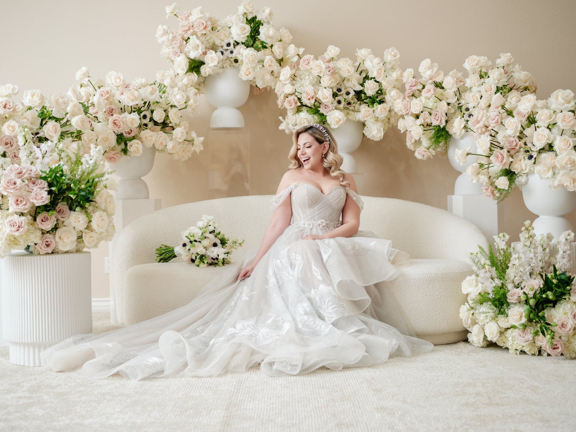 Eliz seated in her wedding gown before a wall of white flowers