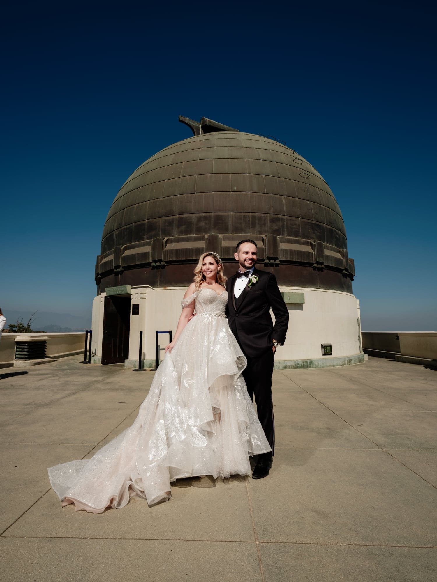 Eliz and Haig standing beneath the Griffith Observatory dome in their wedding attire