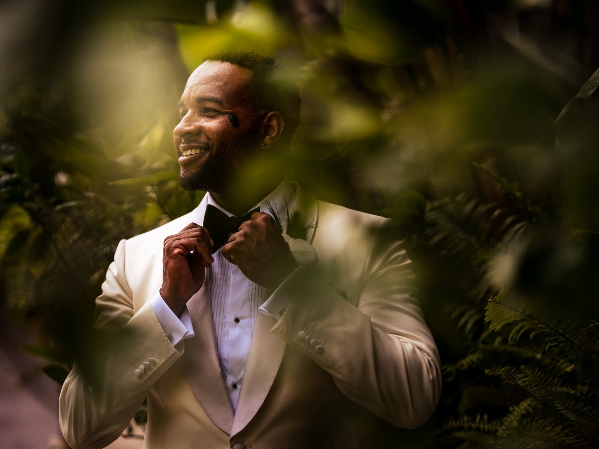 One groom standing in garden light in a white dinner jacket at Greystone Mansion
