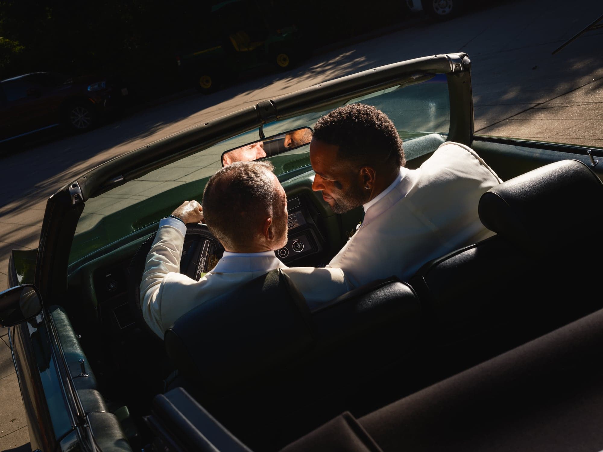 CJ and Rex seated together in a vintage convertible after their ceremony