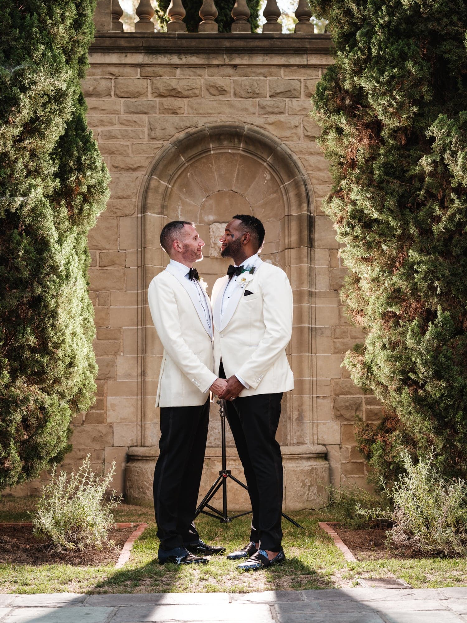 CJ and Rex standing together beneath a stone arch at Greystone Mansion in white dinner jackets