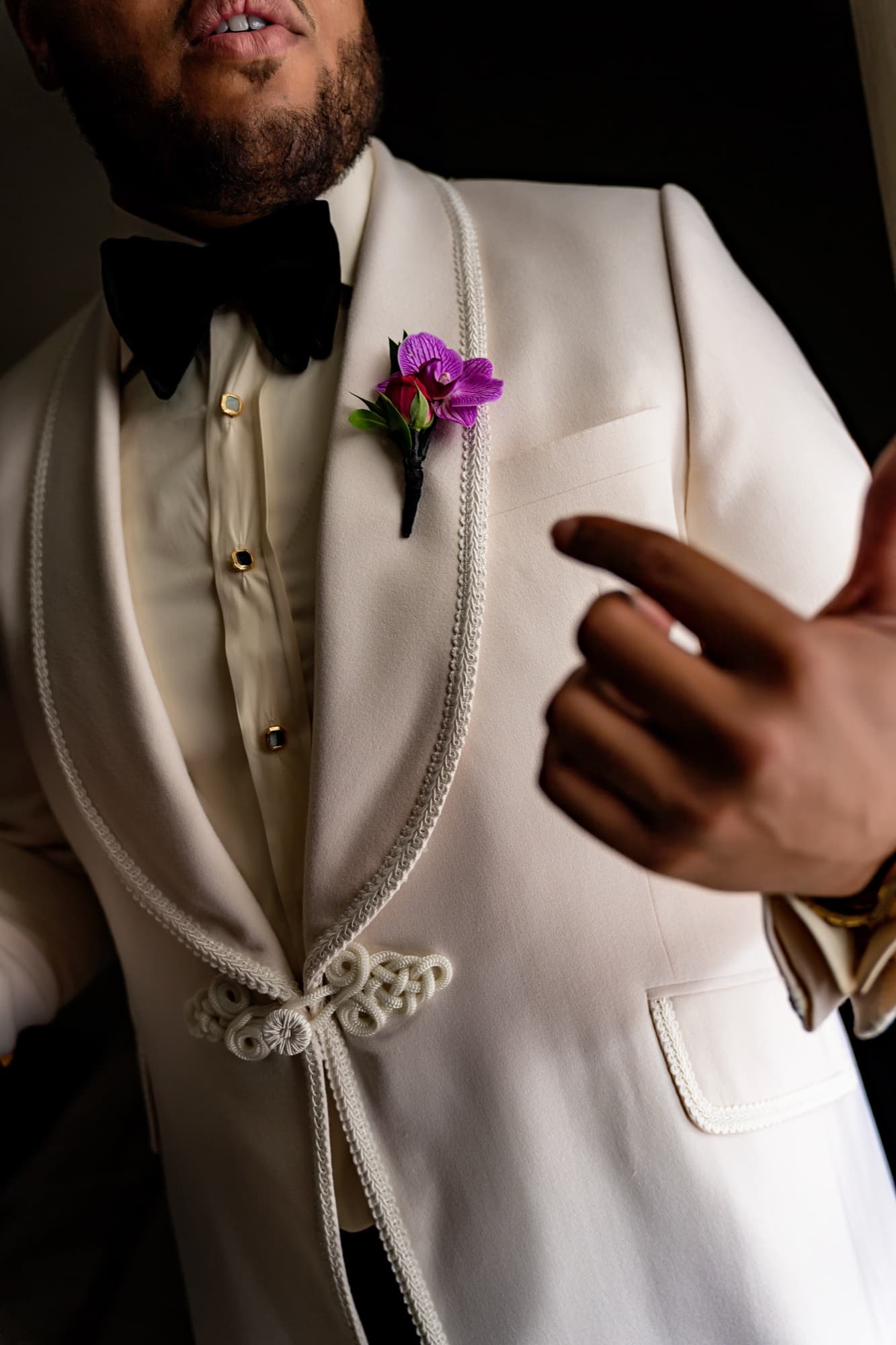 Close-up of Jarell's white shawl-collar dinner jacket with black bow tie and orchid boutonniere