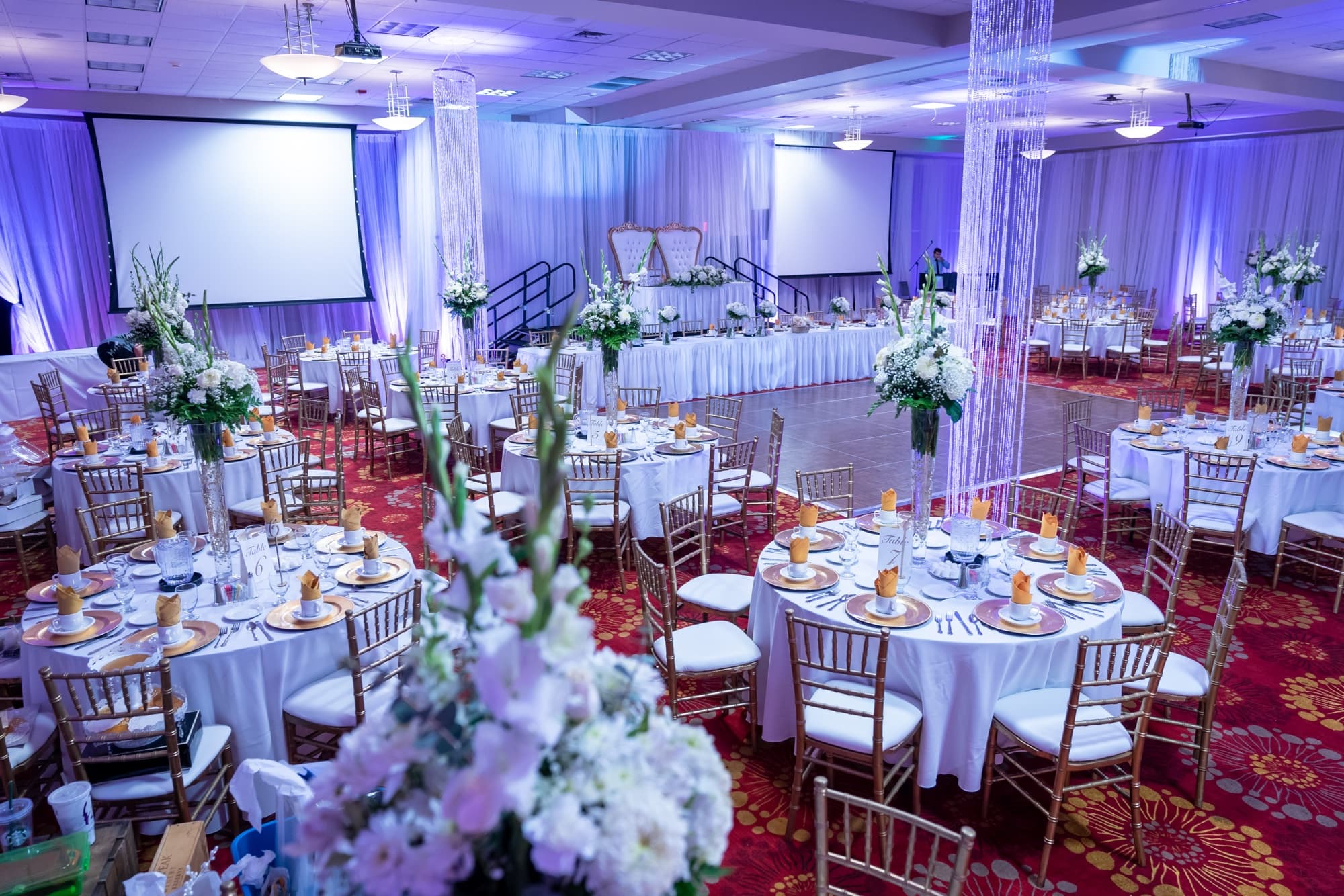 The Hilton Garden Inn Victorville ballroom set for the reception with white florals, throne chairs, and purple uplighting