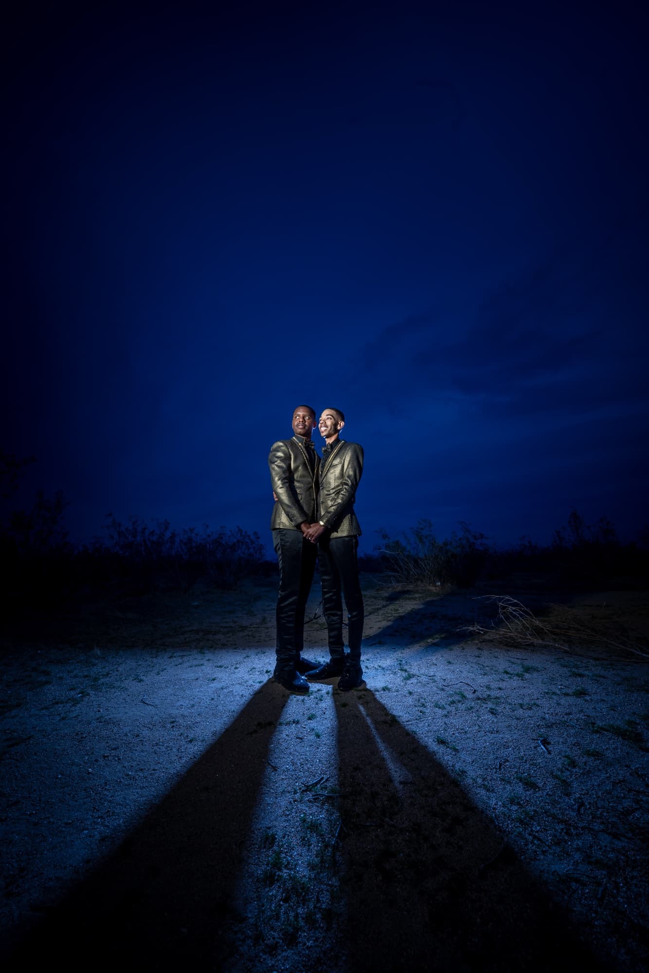 Anthony and Desmond standing together in gold jackets in a pool of light in the desert at blue hour near Victorville