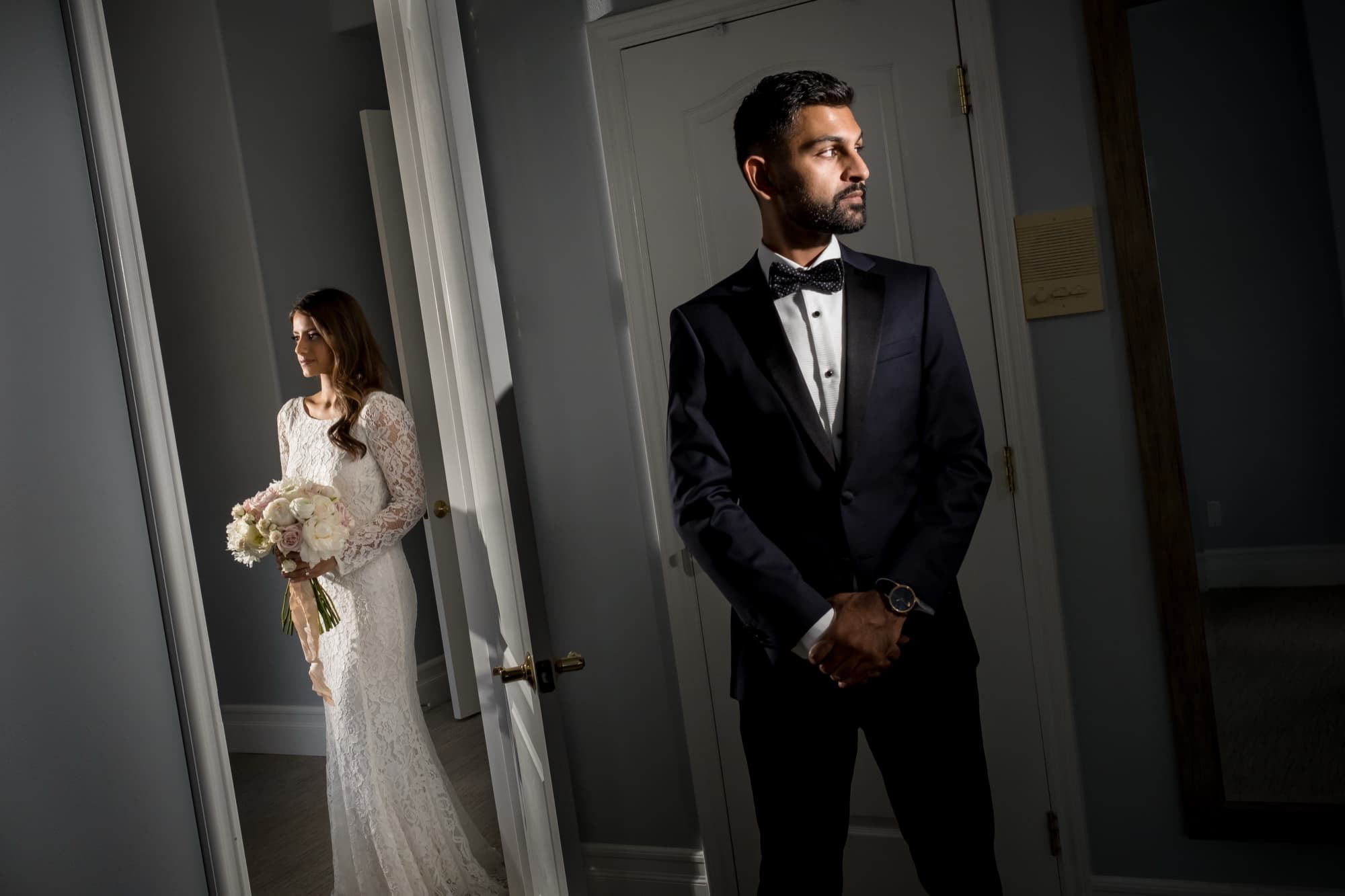 Noor and Sheazad each standing in dramatic doorway light before their intimate wedding ceremony