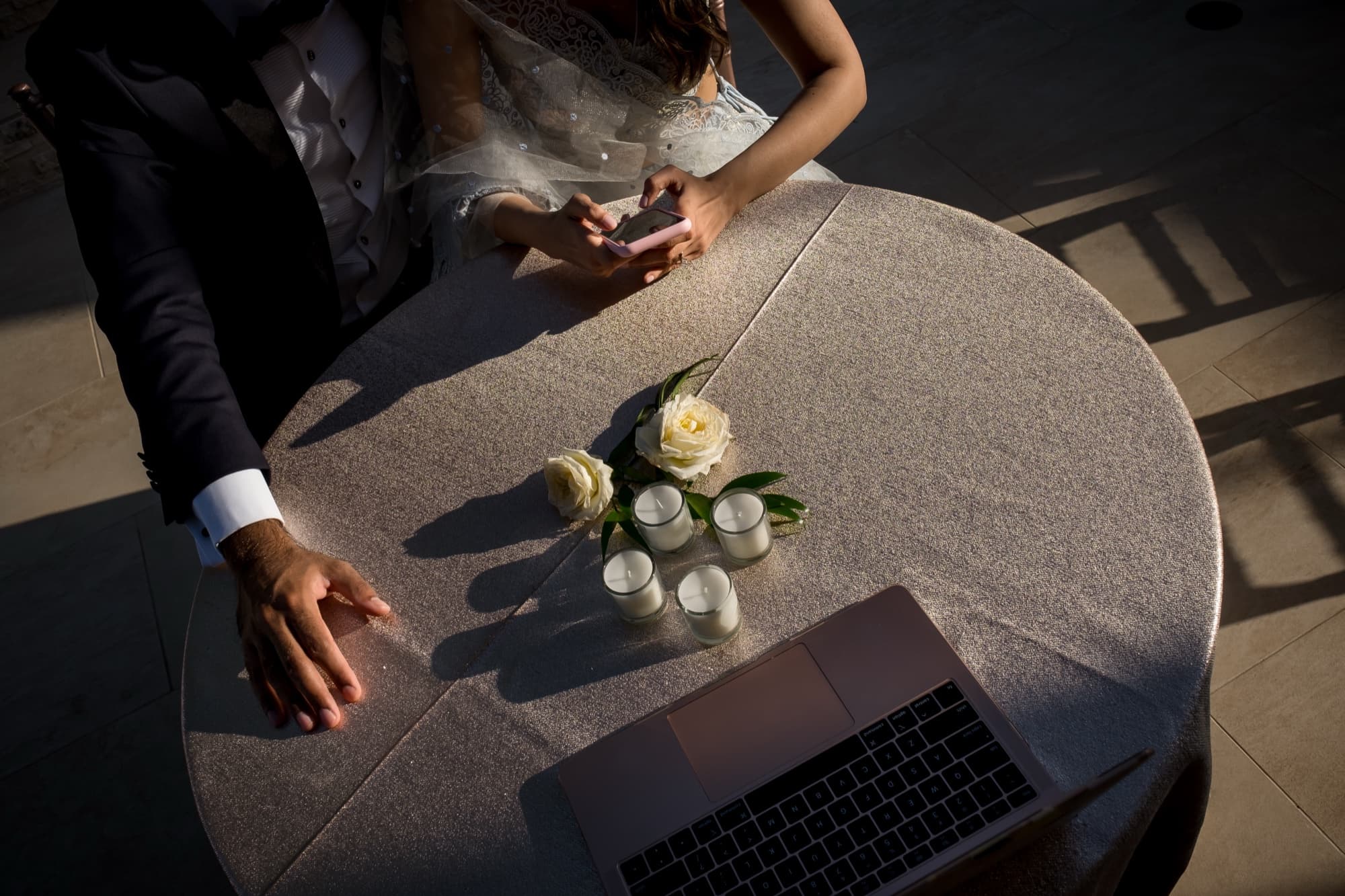 A laptop on a linen table beside a single white rose, carrying the ceremony to family joining by video