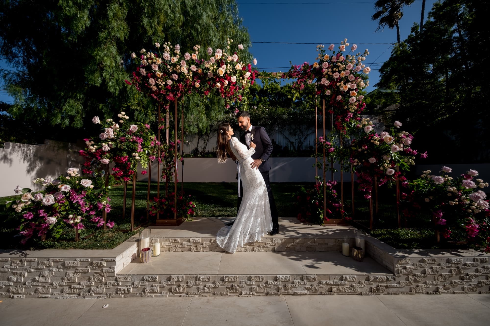 Noor and Sheazad dipping for a kiss beneath a rose and bougainvillea arch at their intimate Los Angeles garden wedding, photographed by Michael Anthony Photography