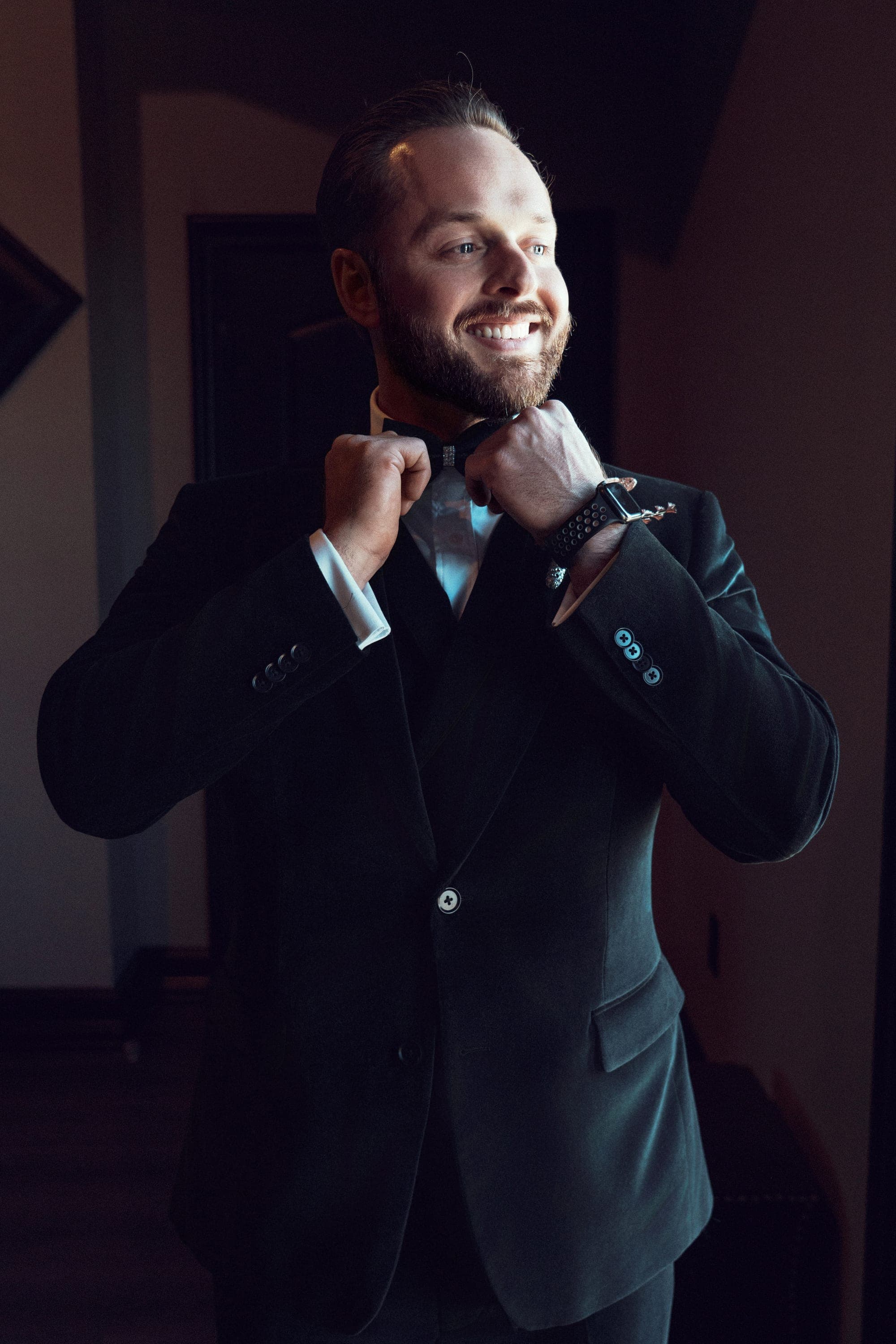Christopher fastening his collar in a black velvet tuxedo