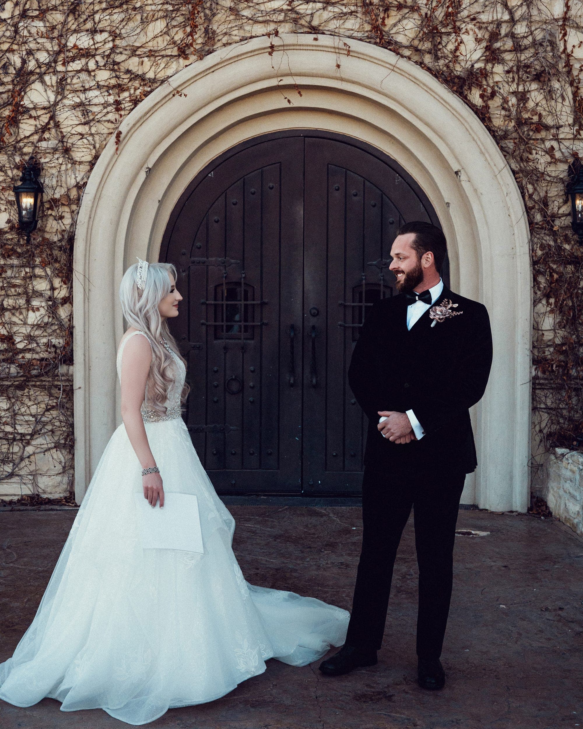 The couple together beneath the arched door, her white gown against the winter ivy