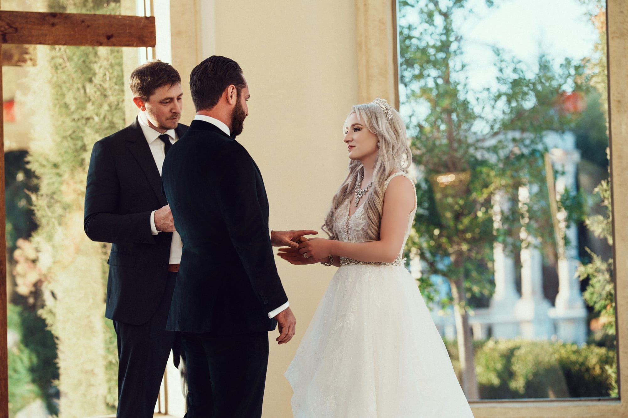 Carly and Christopher exchanging vows before the cross in the chapel's window light