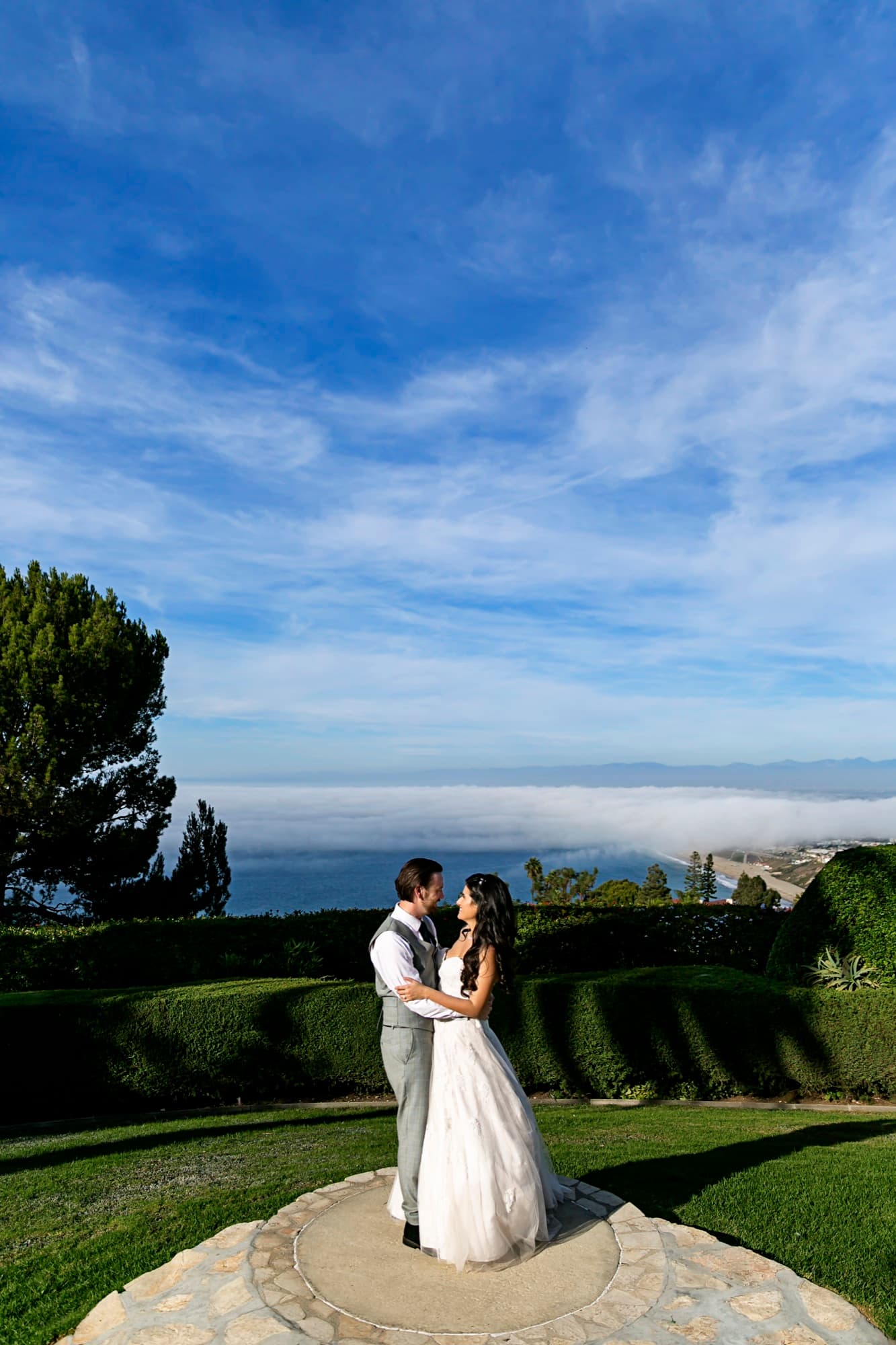 Stephanie and Josh embracing on the stone overlook at La Venta Inn with fog over the Palos Verdes coast behind them