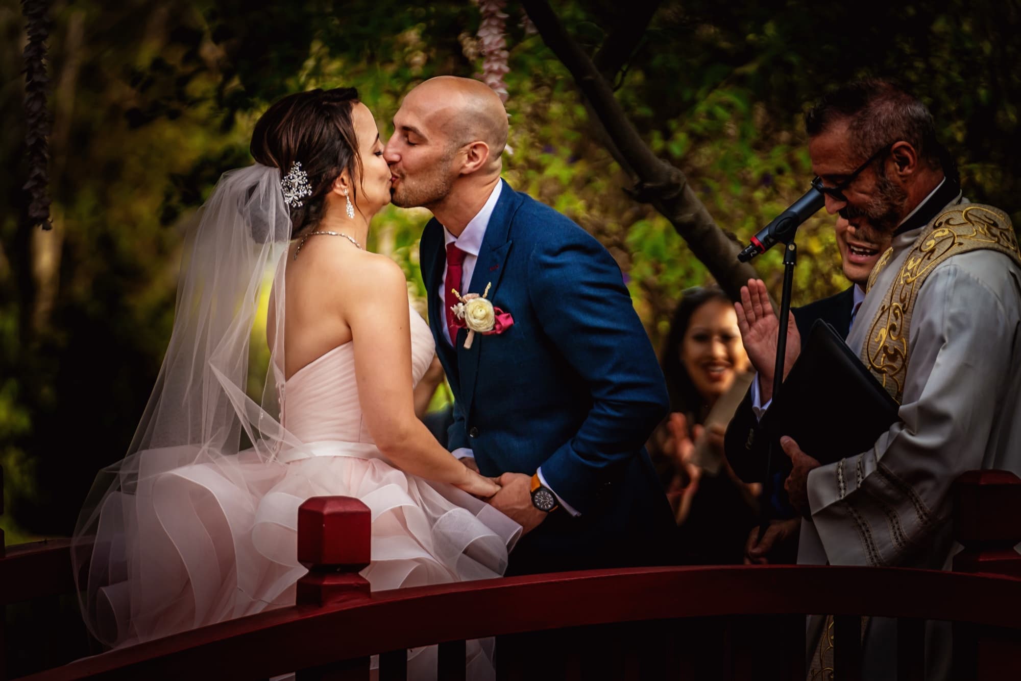 First kiss on the red bridge as the officiant laughs at Ilene and Ricardo's Langham Huntington Pasadena garden ceremony