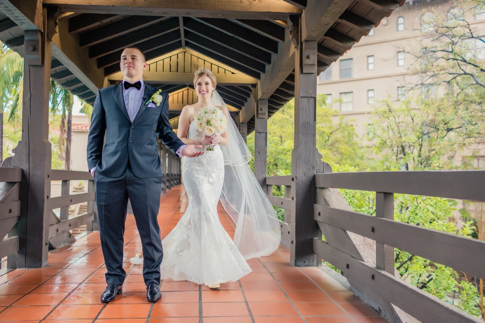 Ilana and Christopher walking across the historic wooden Picture Bridge at The Langham Huntington Pasadena, her veil trailing behind, photographed by Michael Anthony Photography