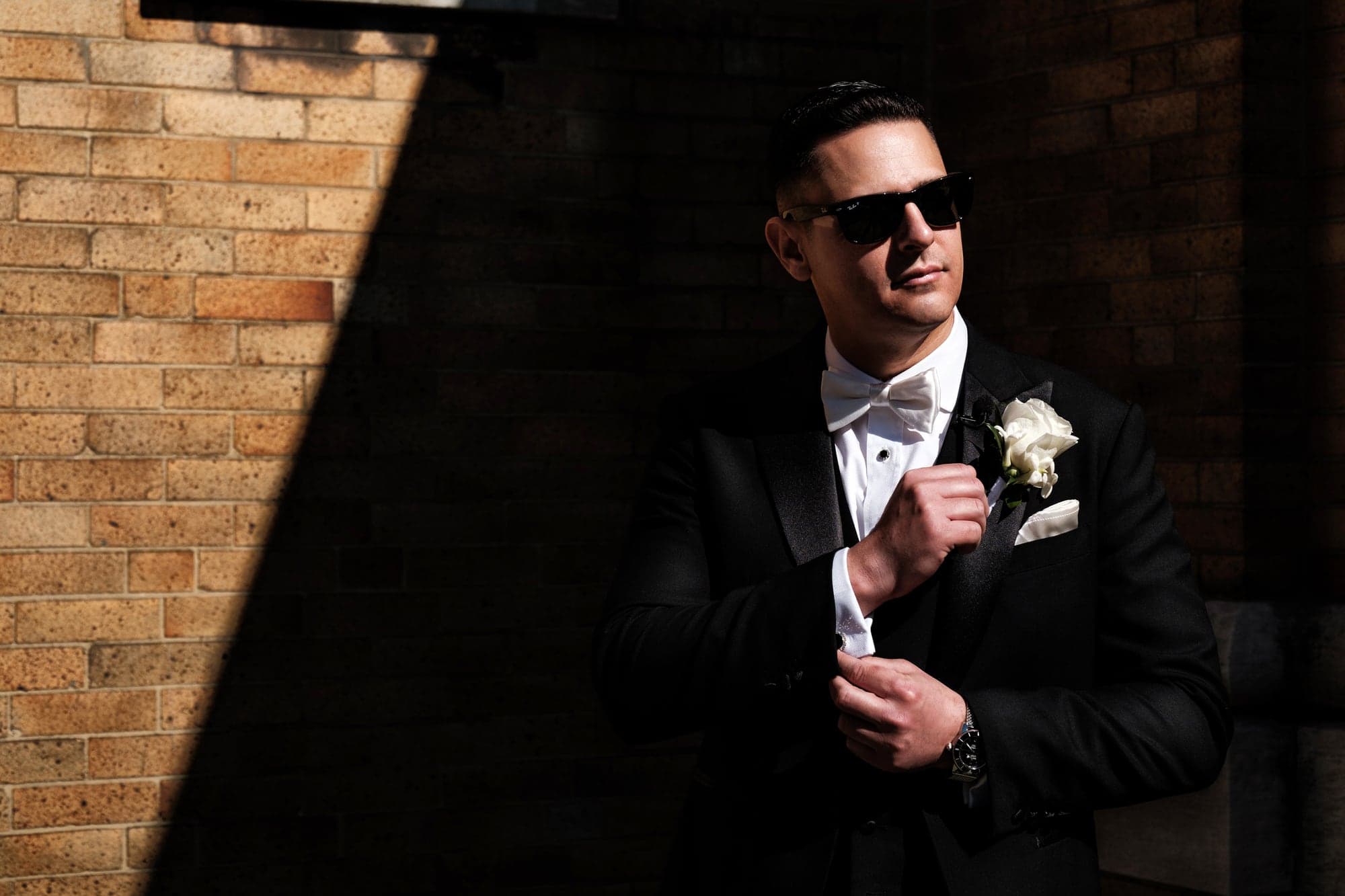 Christopher adjusting his boutonniere in dramatic light before the church ceremony
