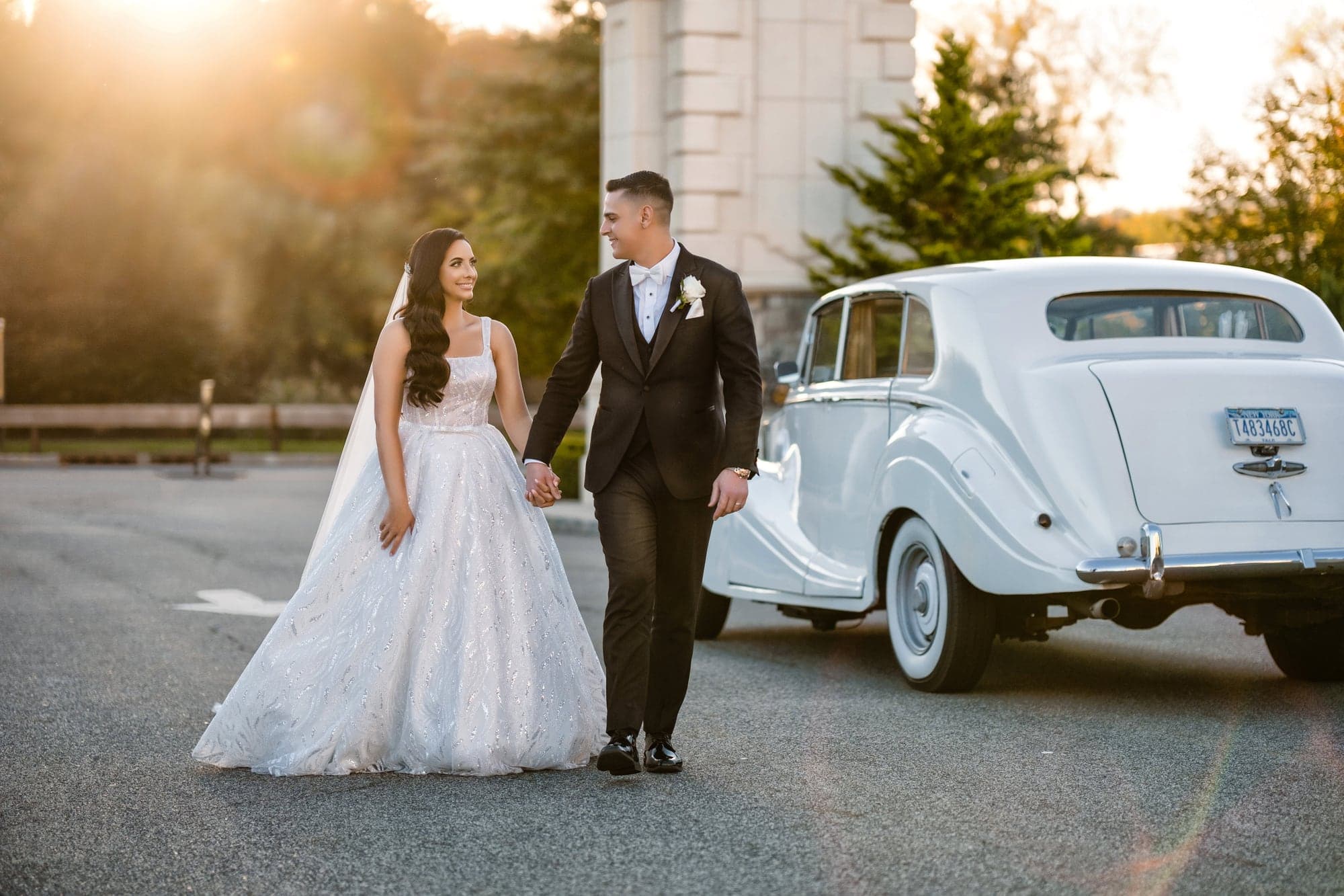 Christopher and Piera embracing beside their vintage car in warm evening light