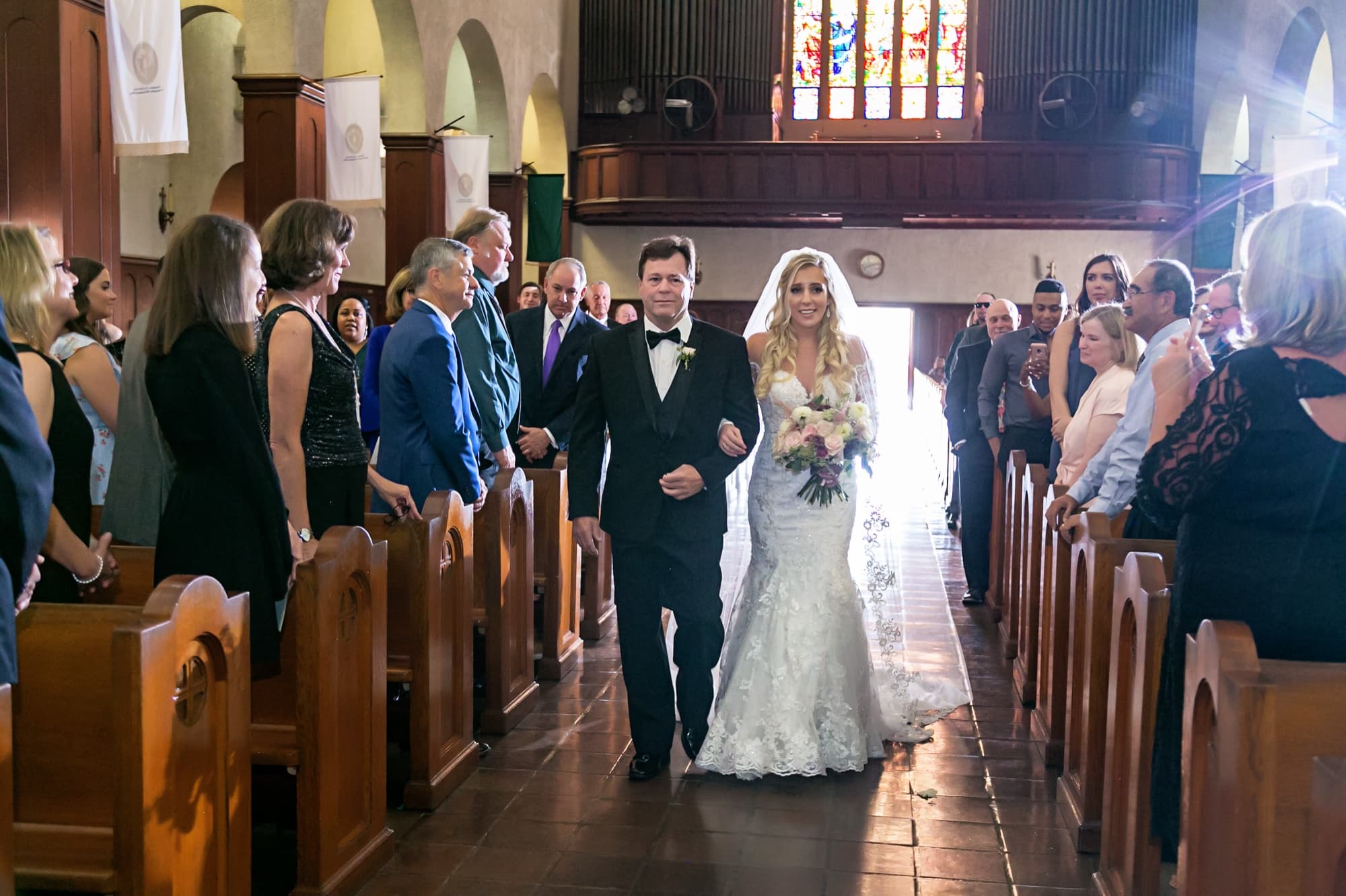 Jaymie on her father's arm walking down the sunlit aisle of Immaculate Conception Church