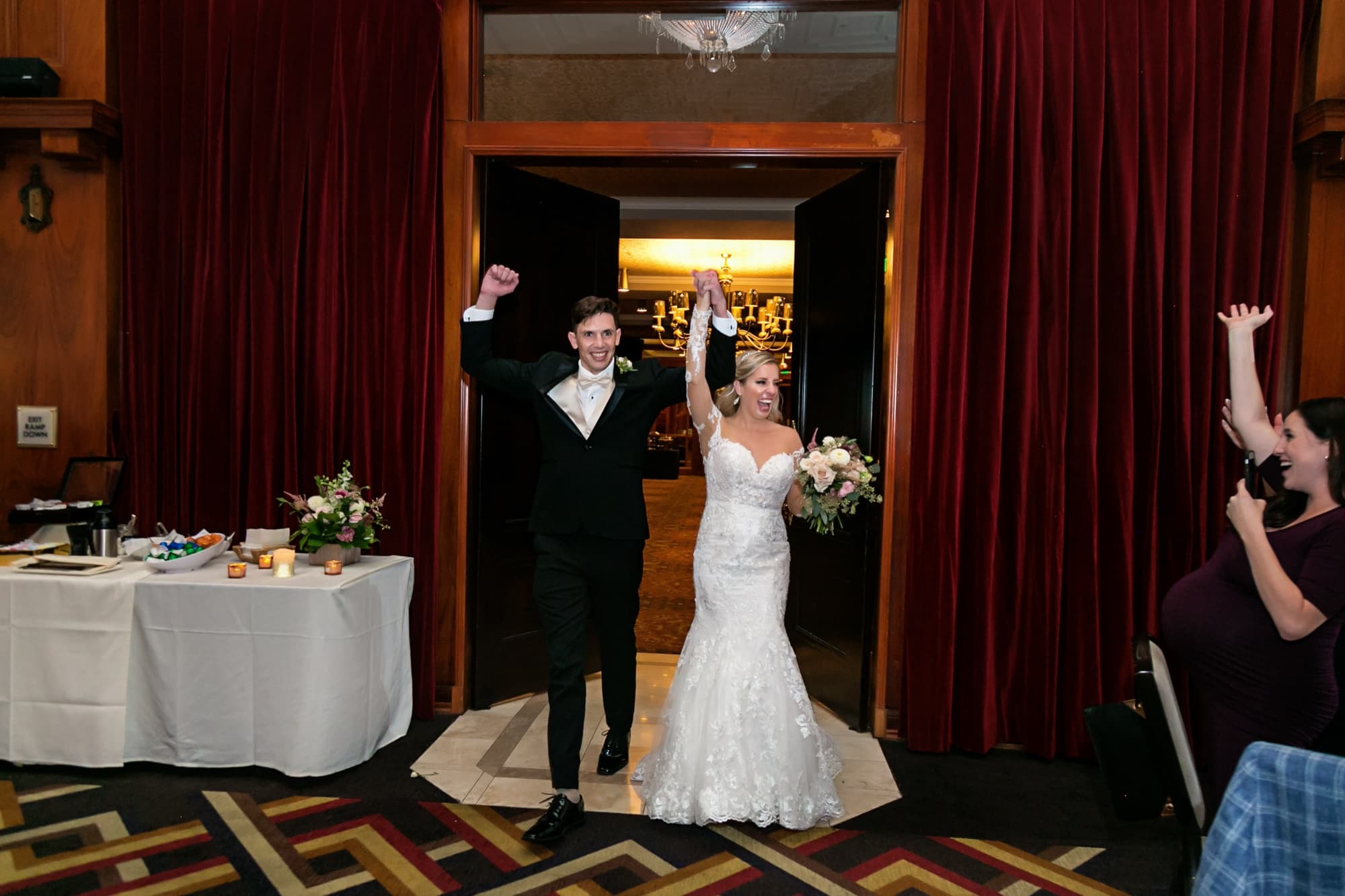 Jaymie and Matt raising their arms during their grand entrance into the wine-red Los Angeles Athletic Club reception