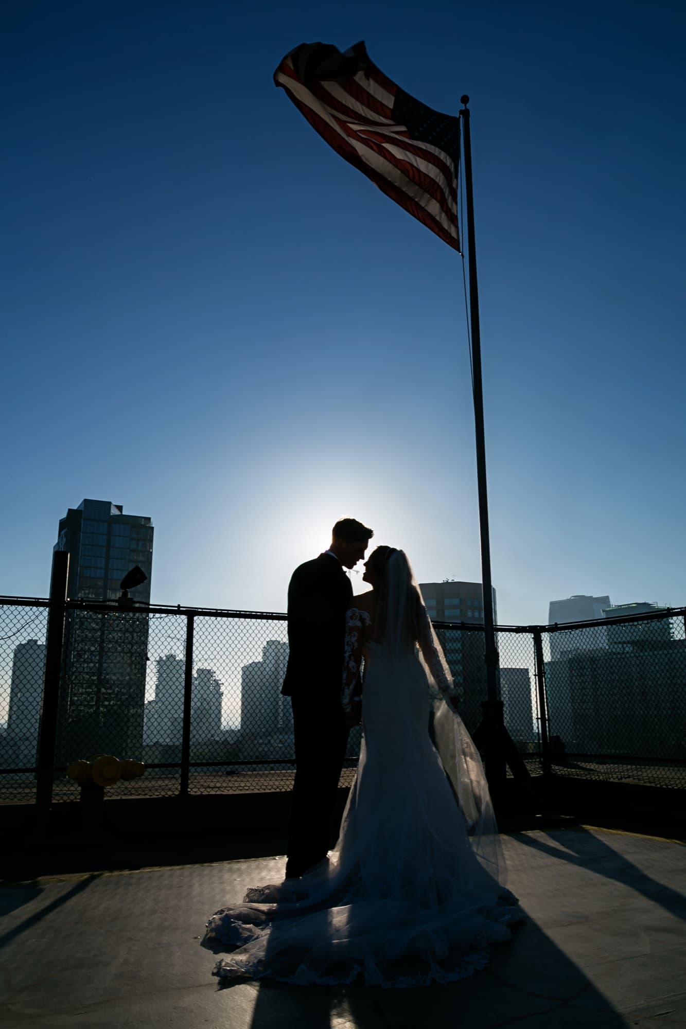 Silhouette of Jaymie and Matt on the Los Angeles Athletic Club rooftop beneath the American flag with the downtown skyline behind them