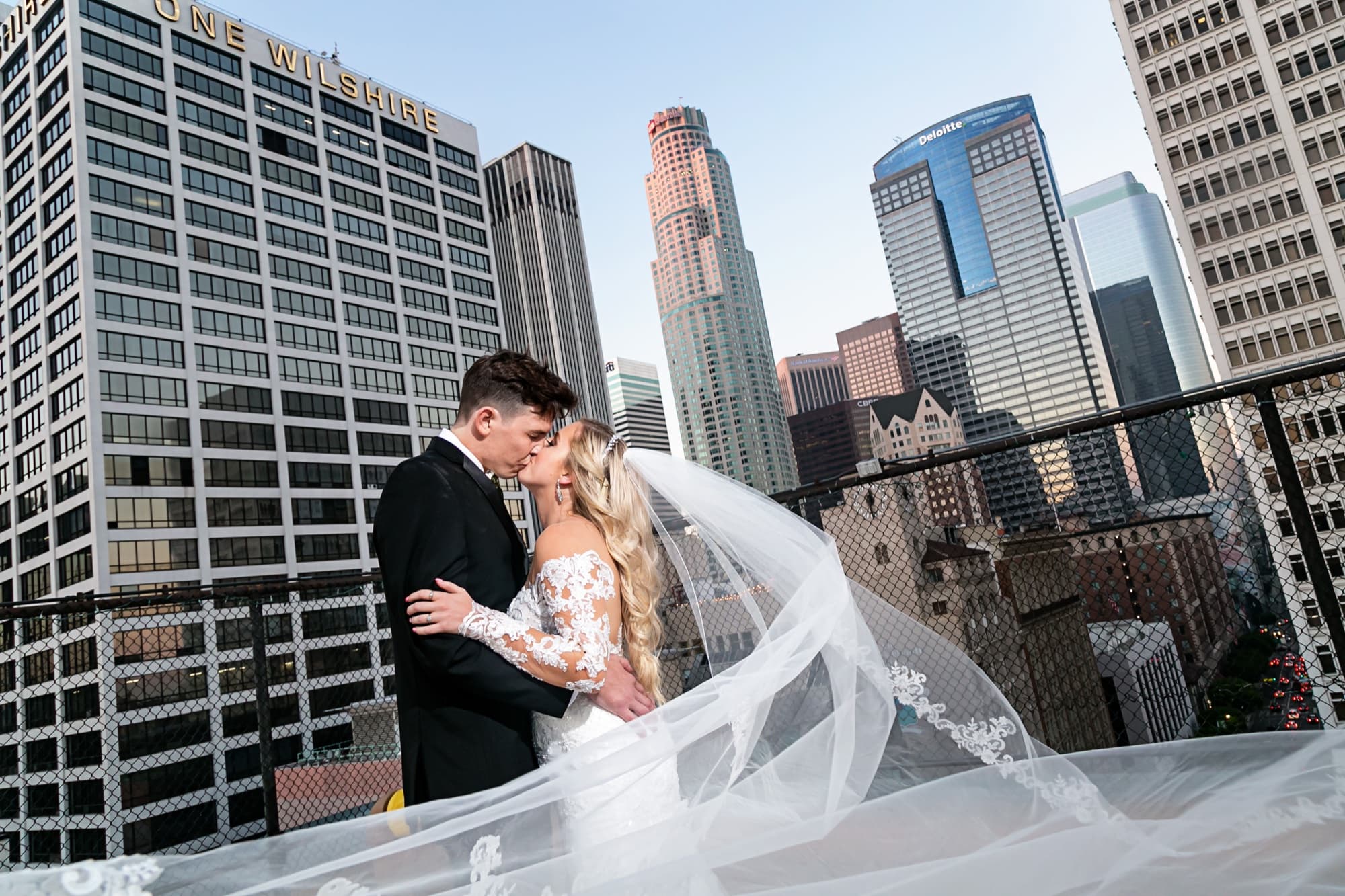 Jaymie and Matt kissing on the rooftop with her veil sweeping across the downtown Los Angeles skyline at golden hour