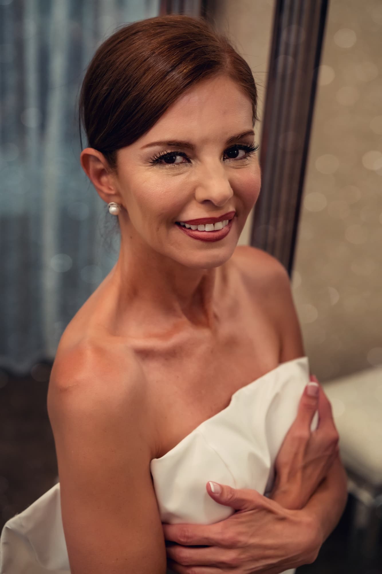 Portrait of Andrea in her boat-neck gown with a low bun and pearl earrings before the ceremony