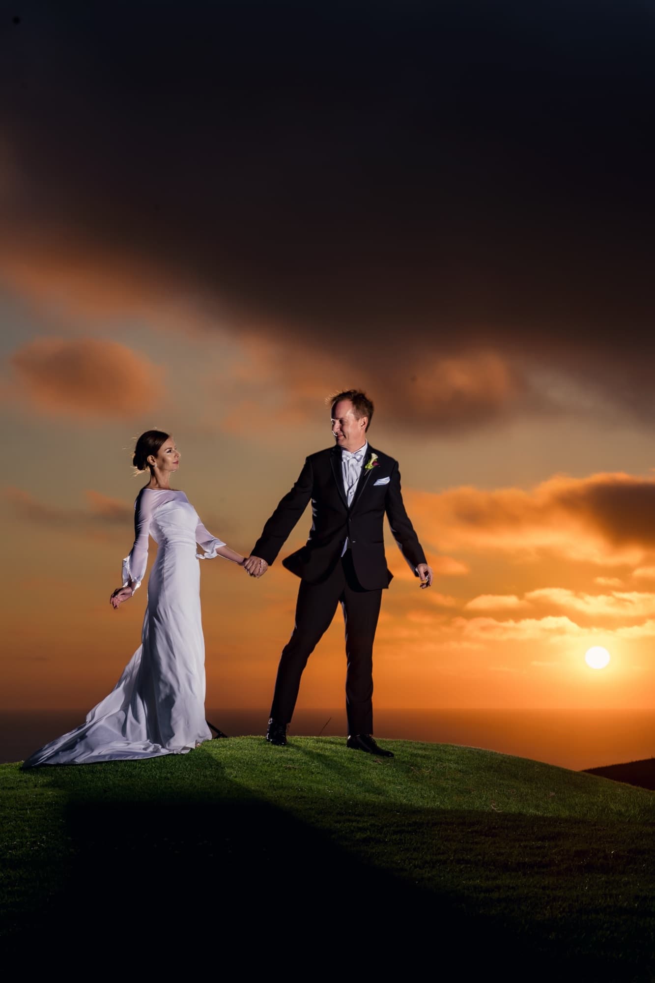 Andrea and John holding hands on the sunset knoll at Los Verdes Golf Course with the sun melting into the Pacific behind them, photographed by Michael Anthony Photography