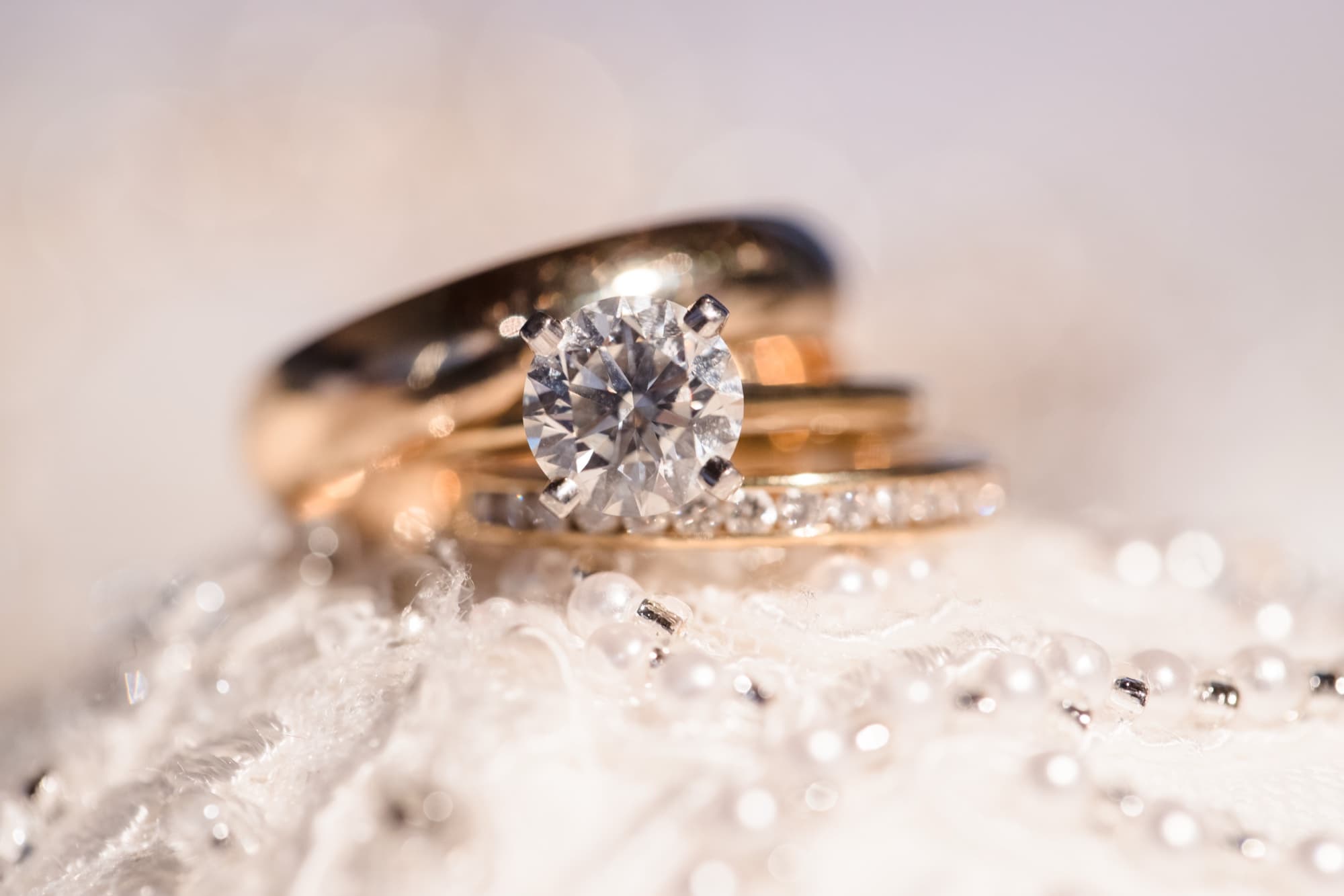 A solitaire diamond engagement ring and diamond band resting on a bed of pearls at a Malibu beach wedding