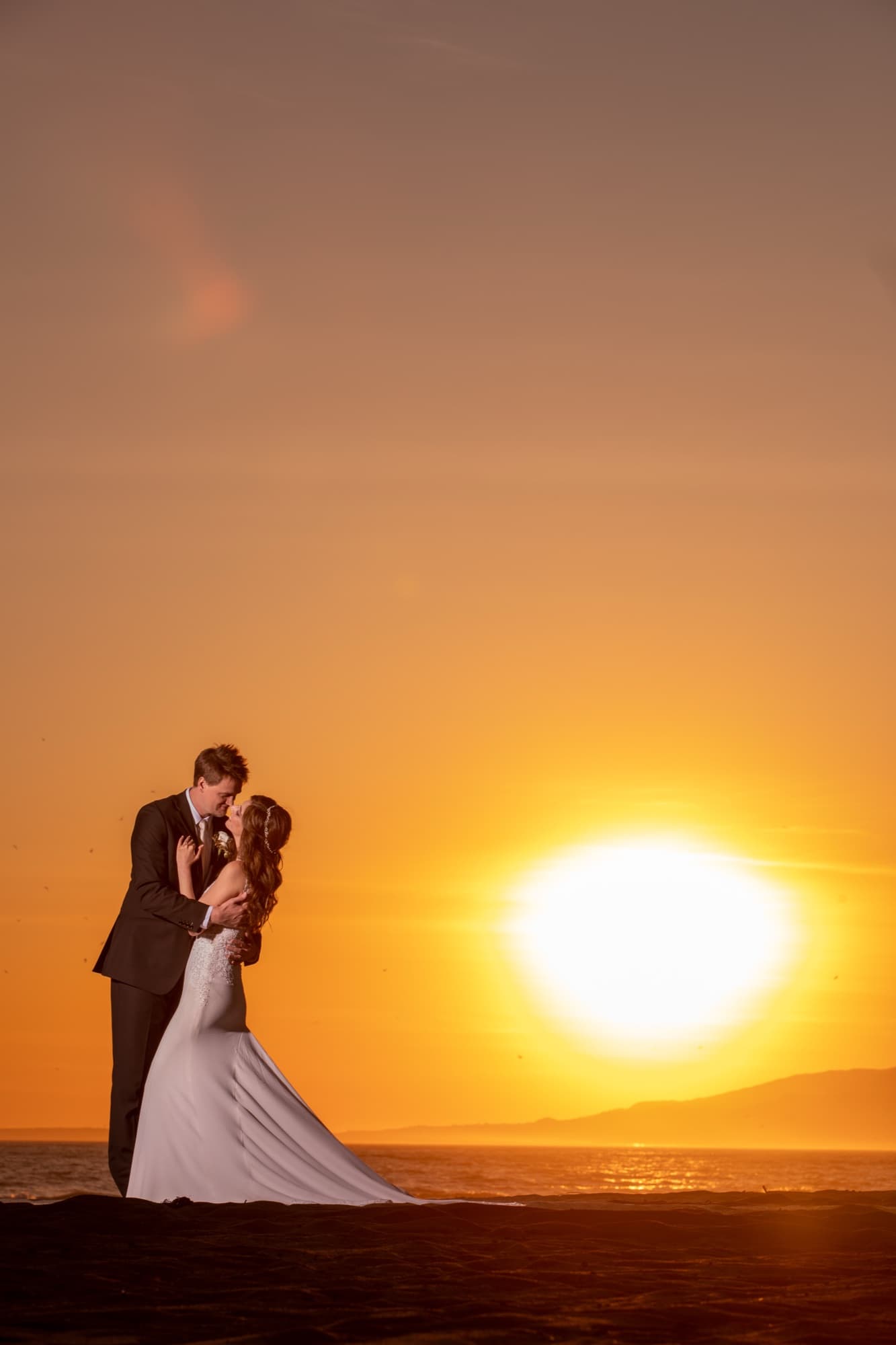 Silhouette of Arta and her groom kissing at the waterline as the sun sets into the ocean in Malibu
