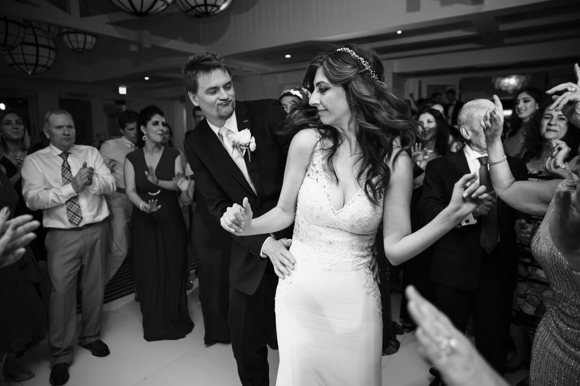 Black and white photograph of Arta and her groom dancing as family circles and claps around them
