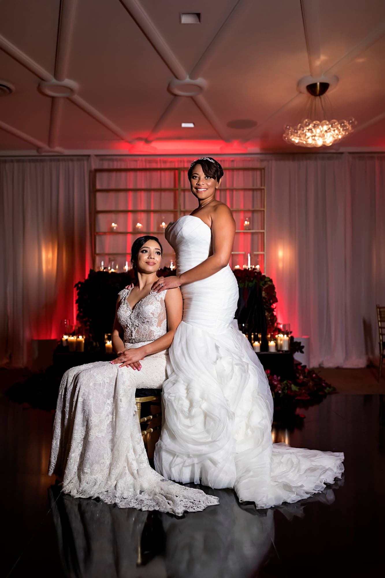 Two brides posing in the red-lit ballroom