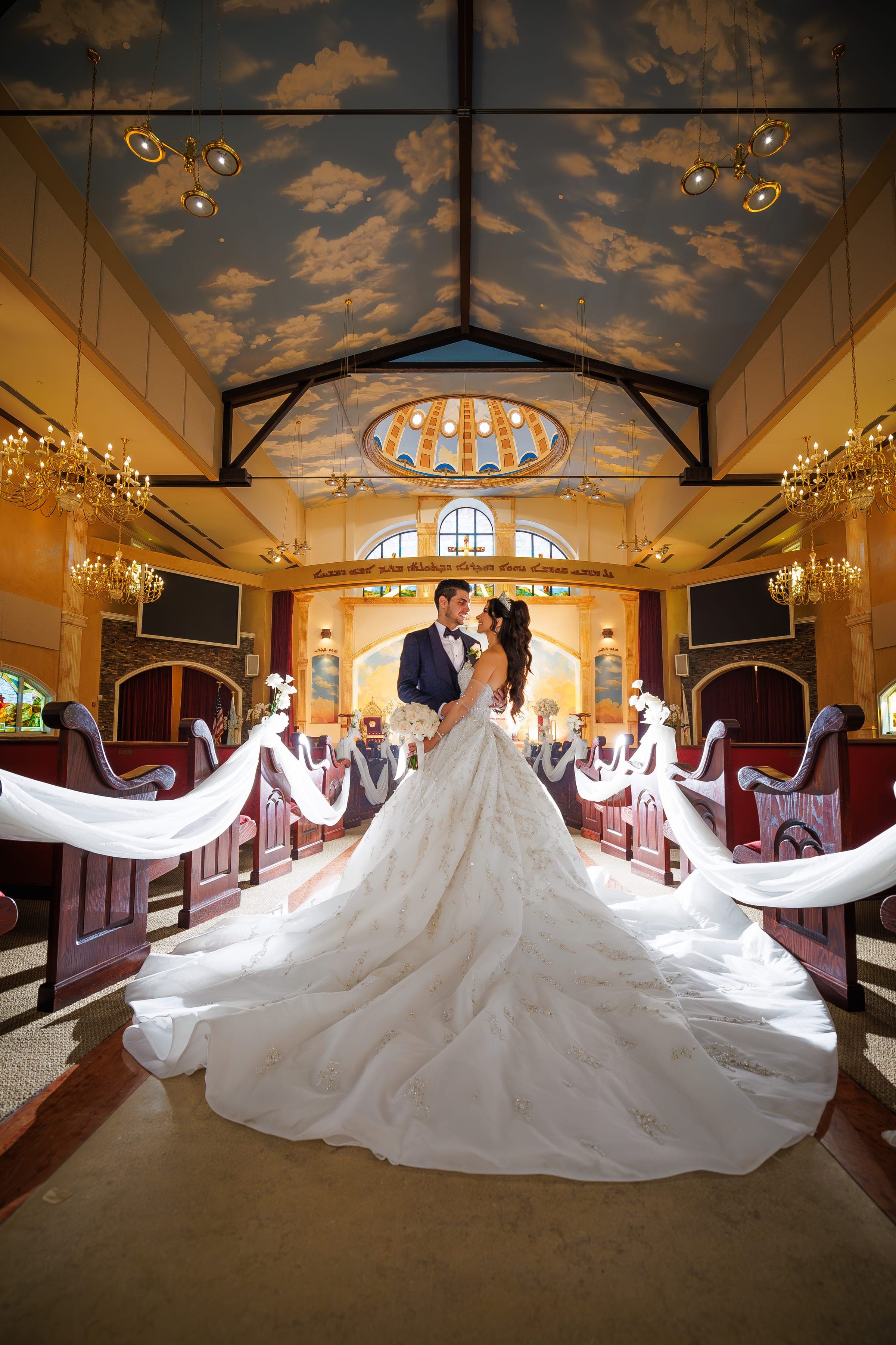 Wide view of the couple facing each other in the church, her gown's train draped over draped pews