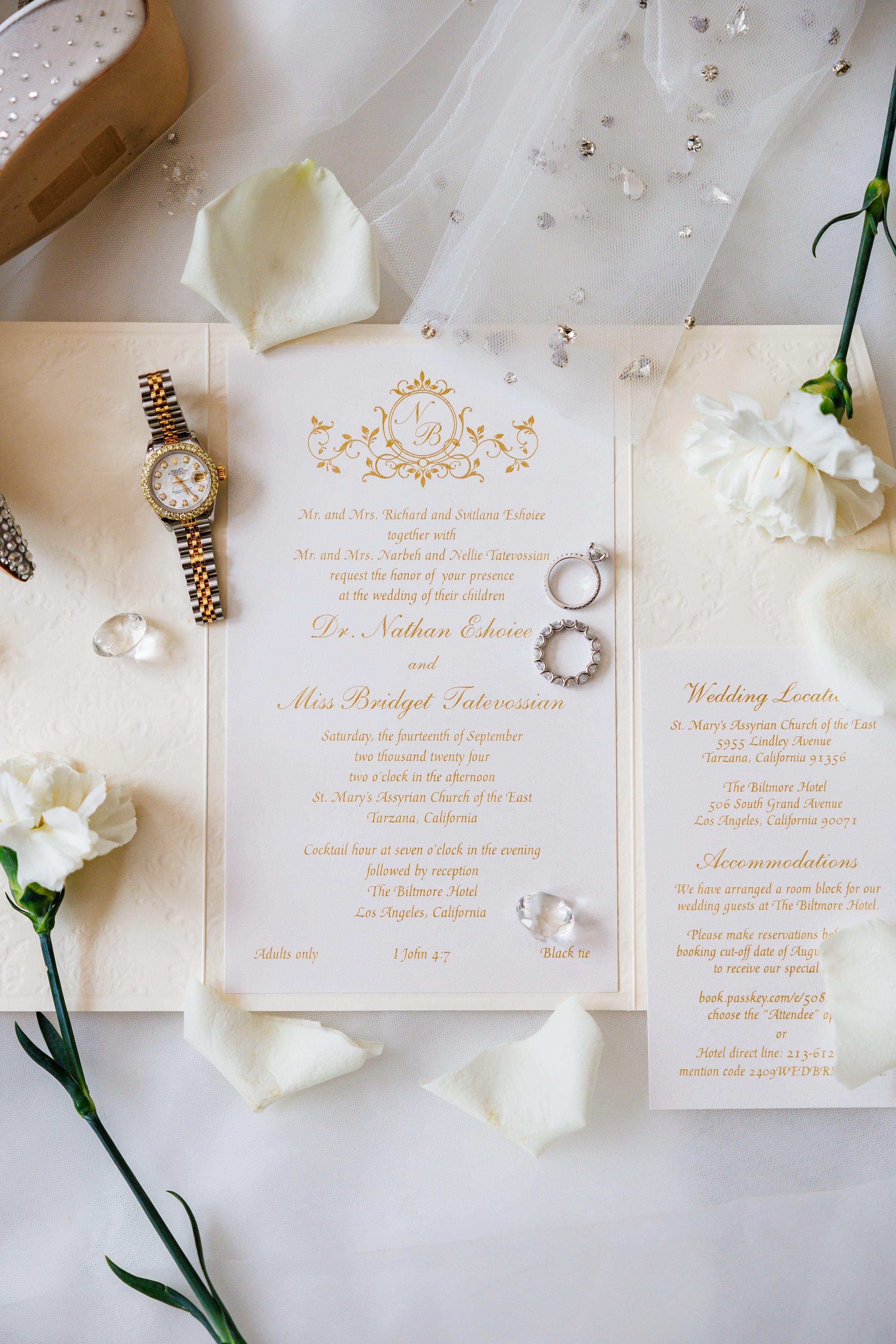 Gold-lettered wedding invitation for Nathan and Bridget displayed with a watch, rings, and white carnations.