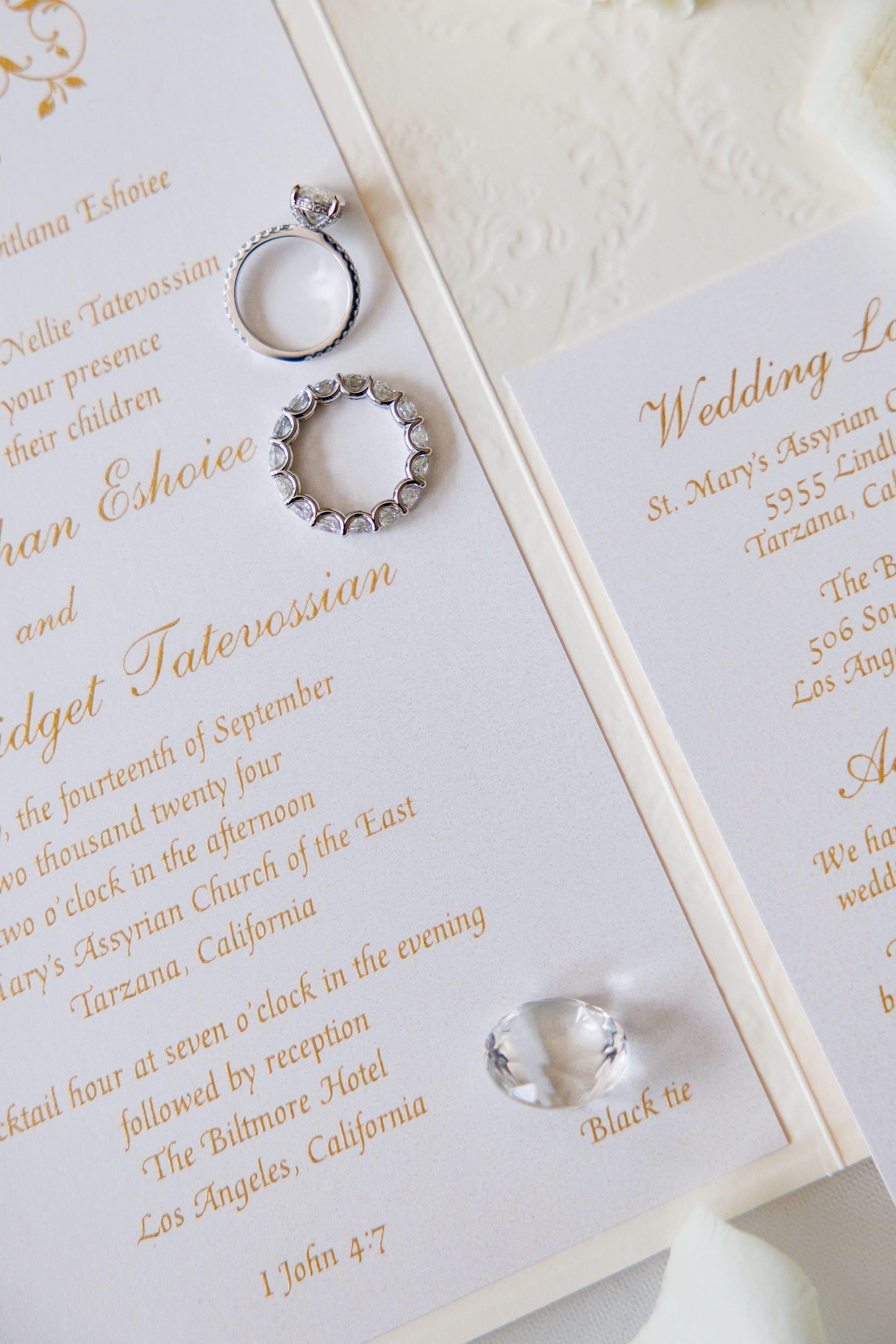 Two diamond rings and a crystal rest atop an elegant gold-script wedding invitation.
