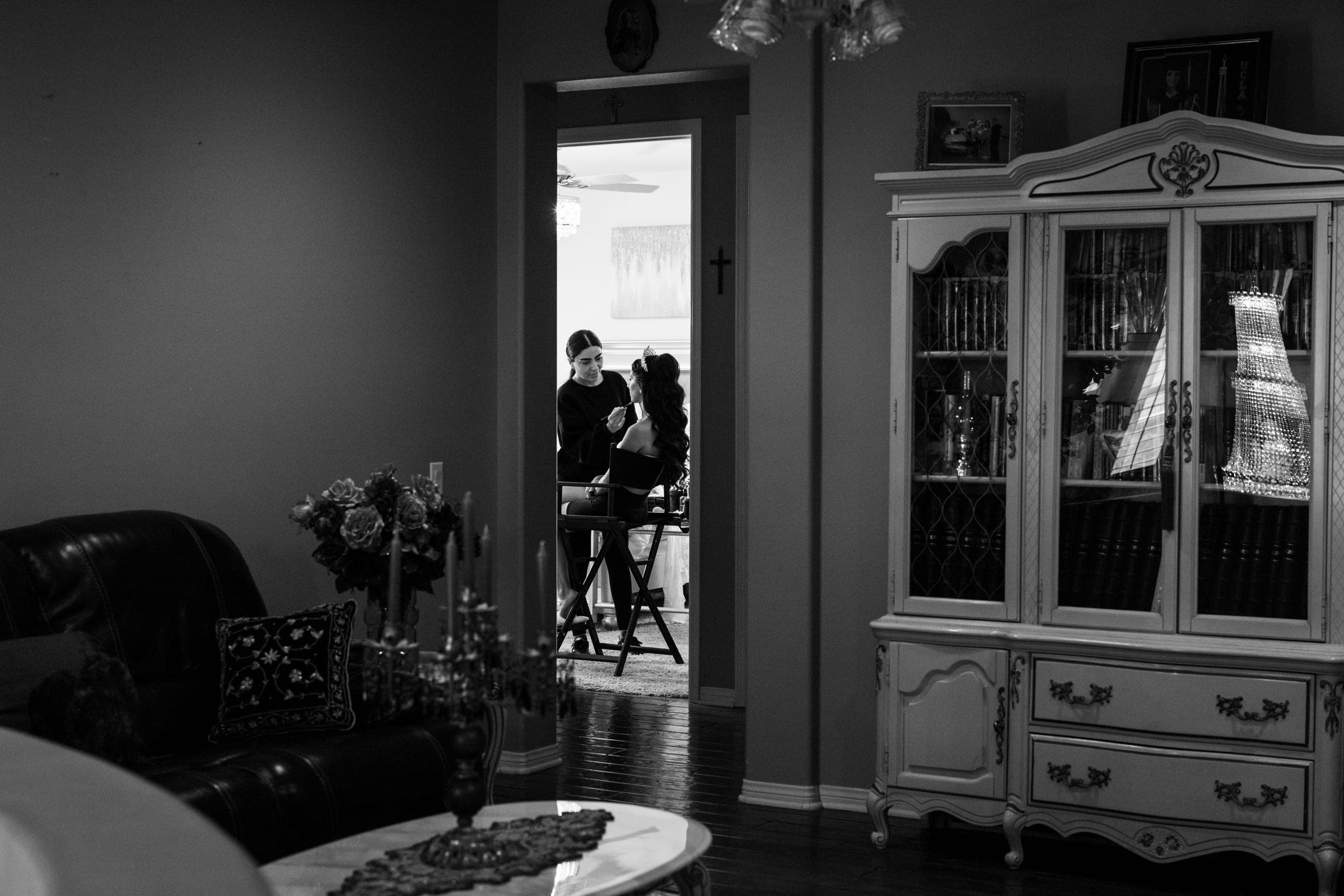 Black and white view through a doorway of two women in a living room with ornate cabinet.