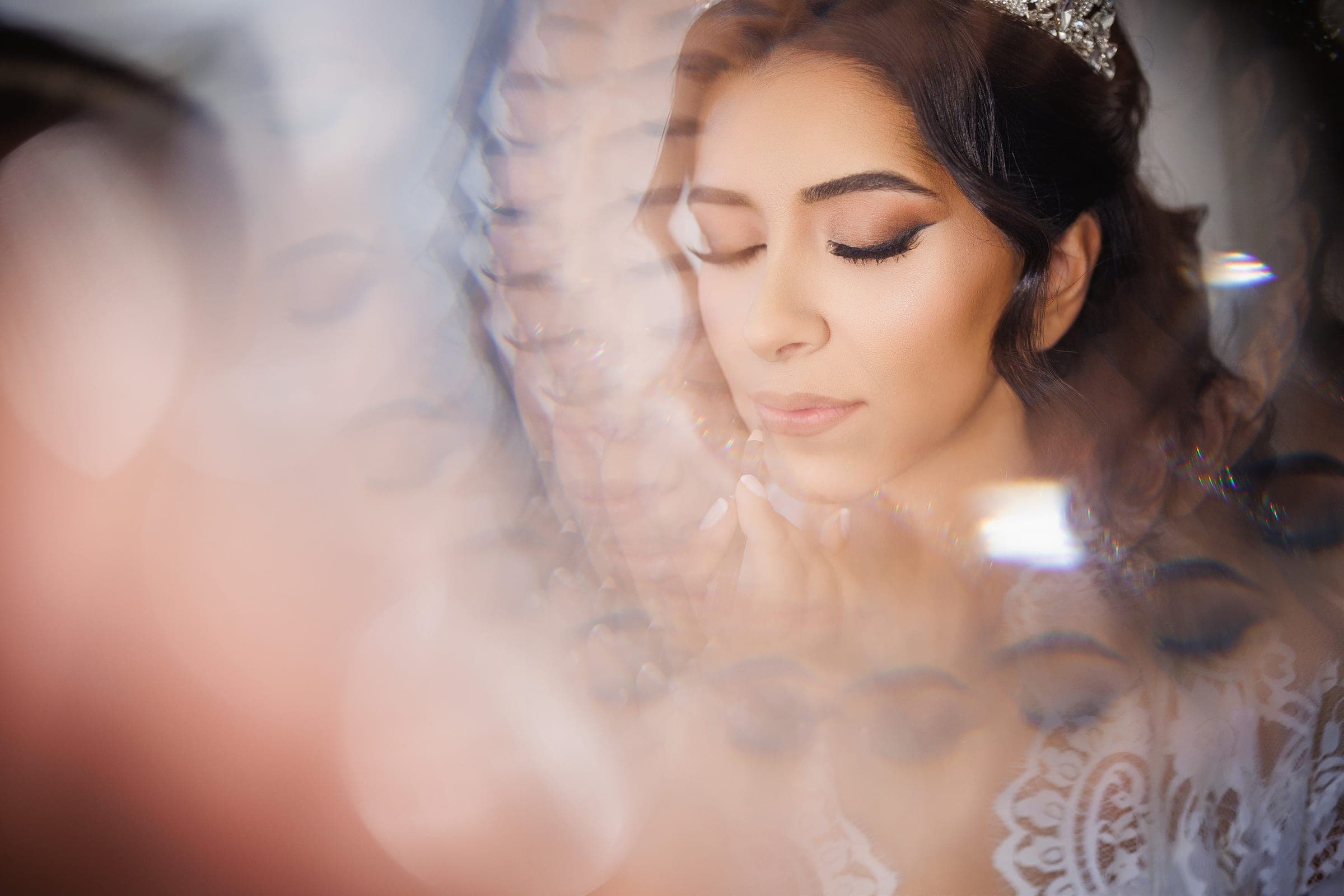 Bride with a tiara and closed eyes rests her chin on her hand, framed by soft bokeh.