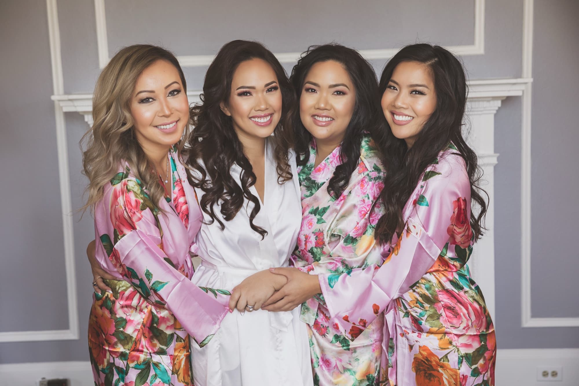 Caroline in a white silk robe laughing with her bridesmaids in floral robes on the wedding morning