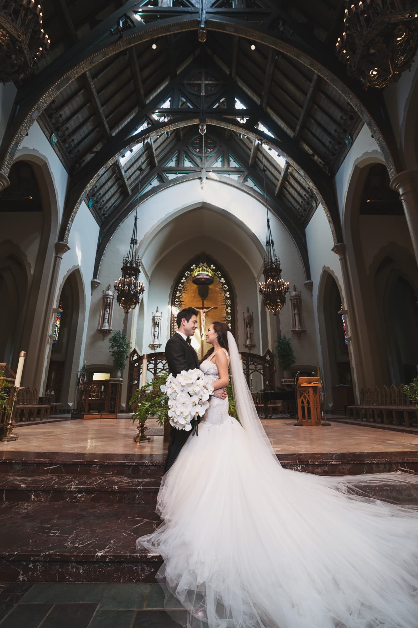 Caroline and Gerald standing together at the altar of a historic Gothic church in Los Angeles with arched timbered ceilings above