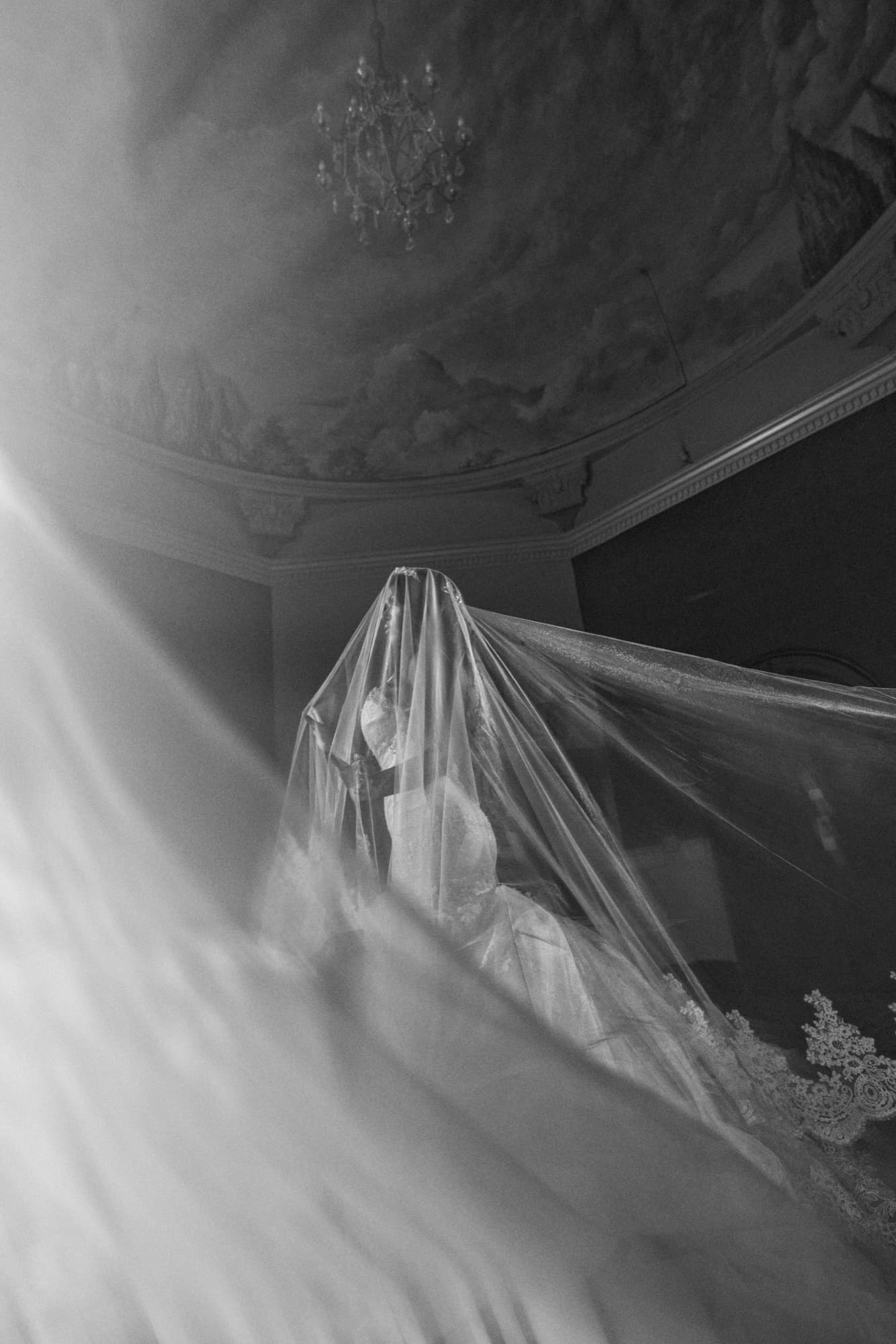 Black and white photograph of the bride's veil cascading down a staircase at the Mission Inn beneath a chandelier