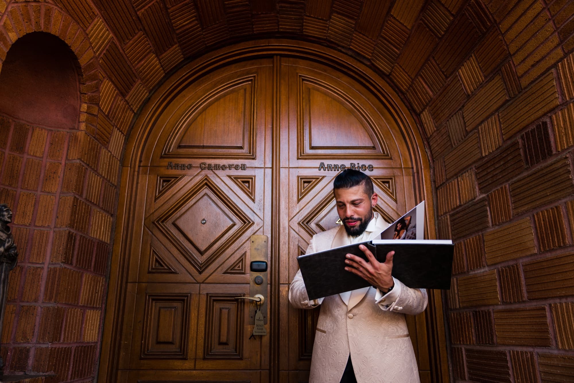 Groom in an ivory tuxedo jacket reading a letter in front of the Mission Inn's carved wooden doors