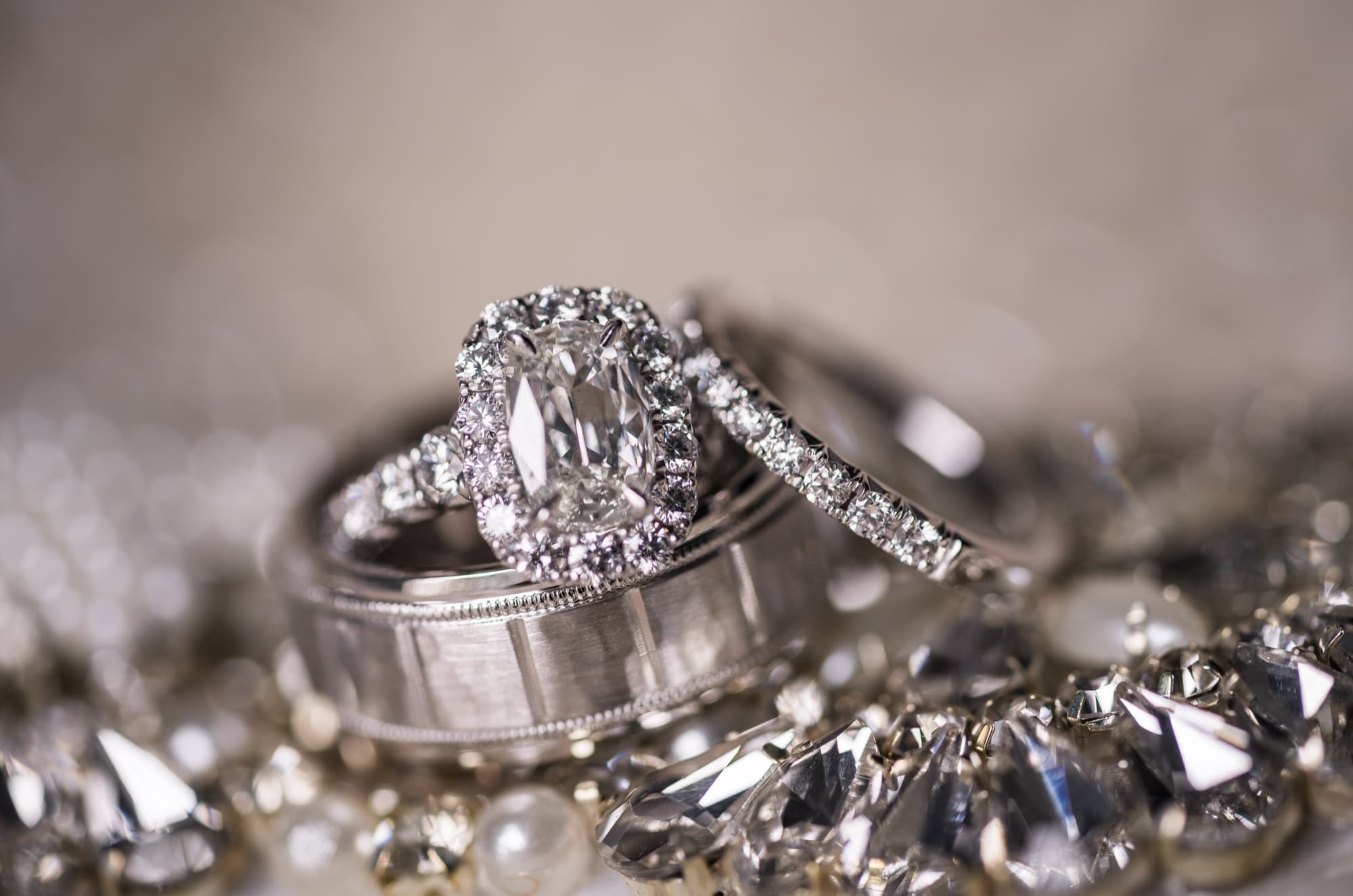 A cushion-halo diamond engagement ring and diamond band resting on a bed of crystals at a Palos Verdes wedding