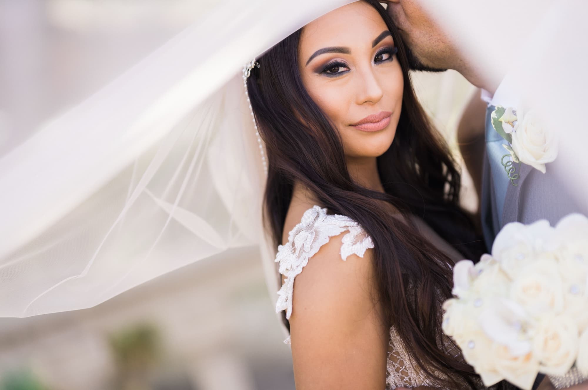 Beauty portrait of Karina with her veil drawn across her shoulder and a white rose bouquet in the coastal light