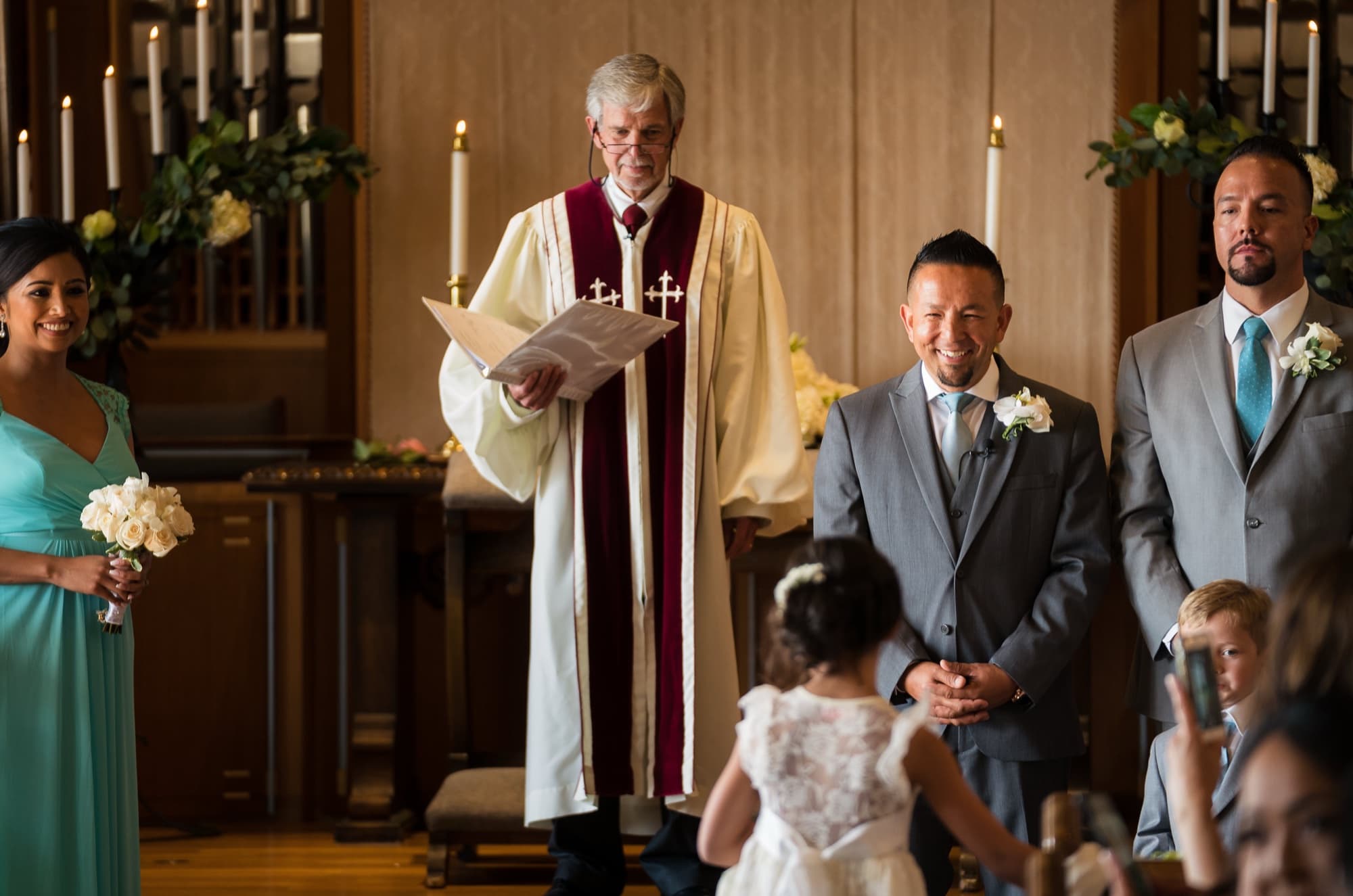 The minister leading the ceremony as Faustino and his groomsmen in grey stand at the altar of The Neighborhood Church