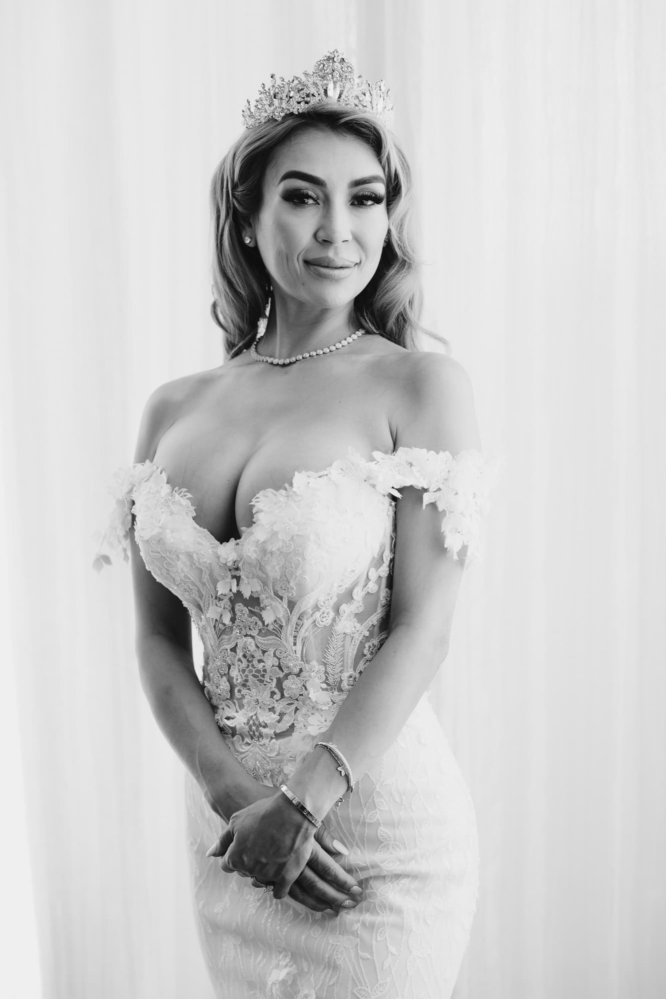 Black and white portrait of Danielle in her crown and off-shoulder lace gown against the bright window drapery