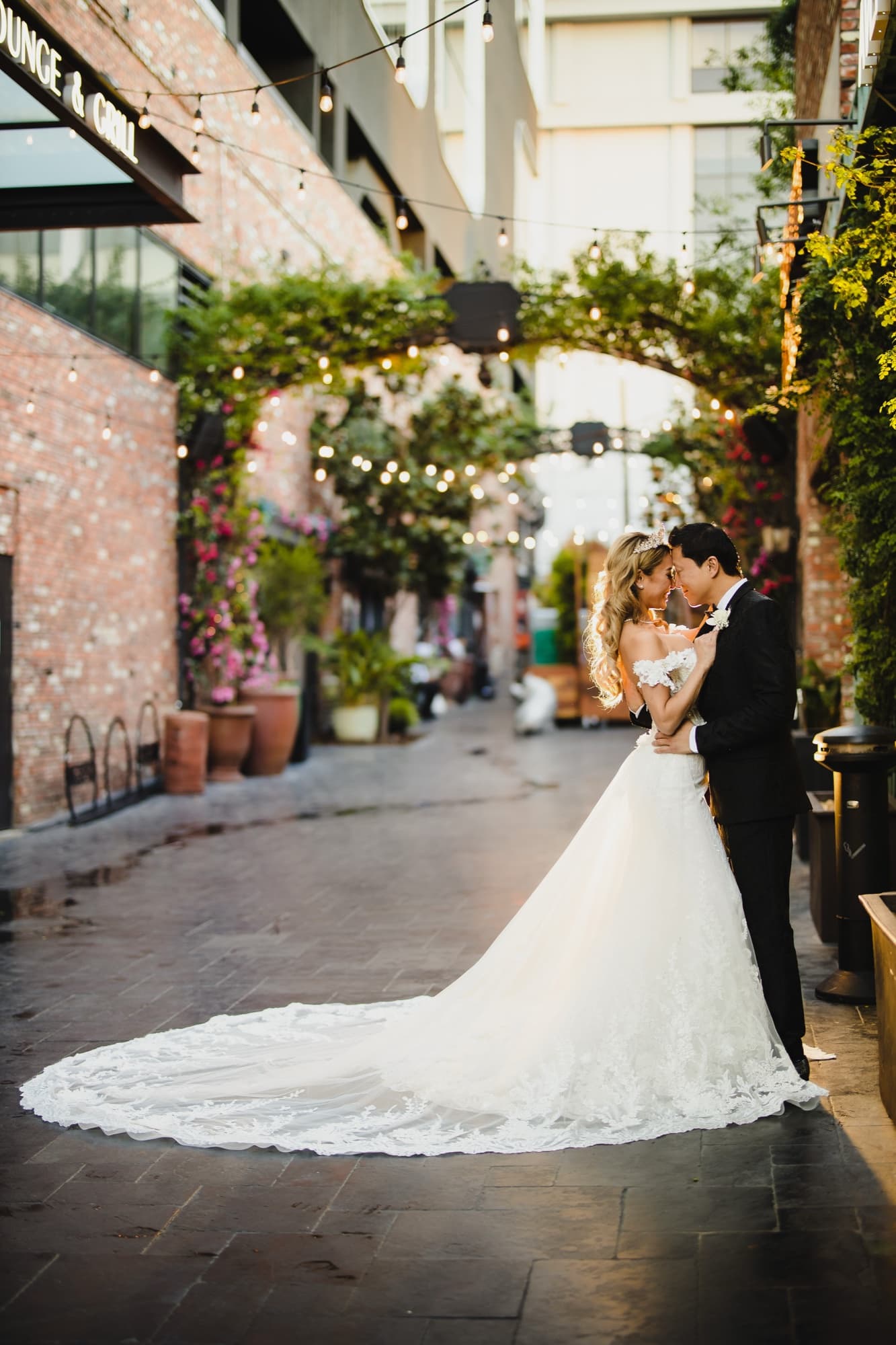 Danielle and Justin kissing in the bougainvillea-draped alley beside NeueHouse, her lace train pooled across the brick
