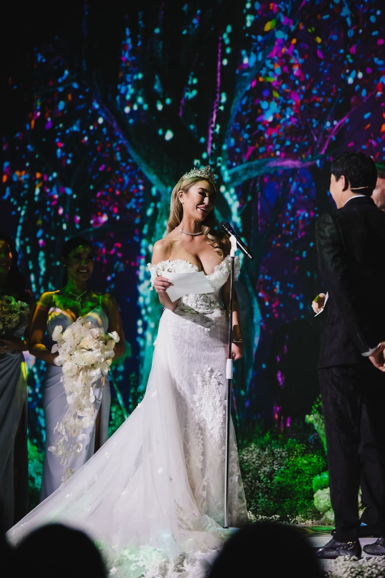 Danielle and Justin exchanging vows on the blossom-dressed stage beneath the projected forest