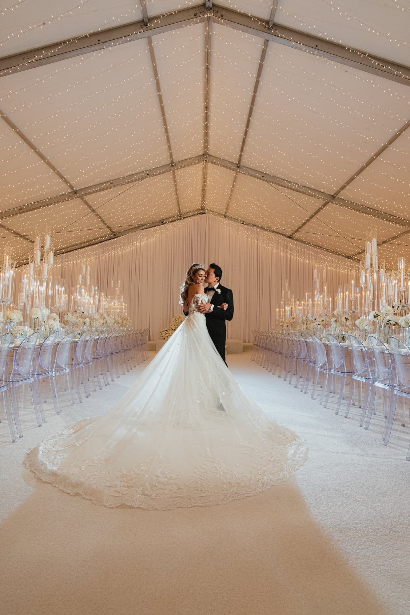 Danielle and Justin embracing in the center of the white-draped reception tent at NeueHouse Hollywood, her cathedral train filling the candlelit aisle, photographed by Michael Anthony Photography