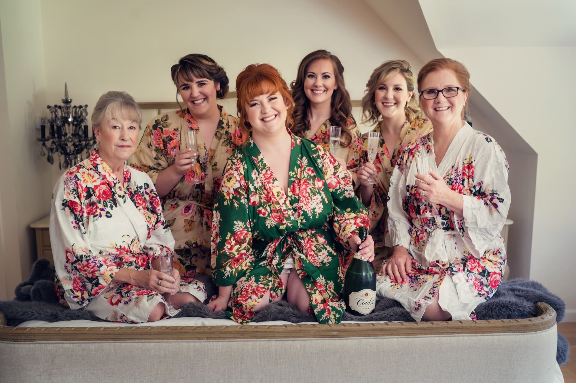 Michelle in an emerald floral robe with her bridesmaids and mothers in blush robes on the window seat at Newhall Mansion