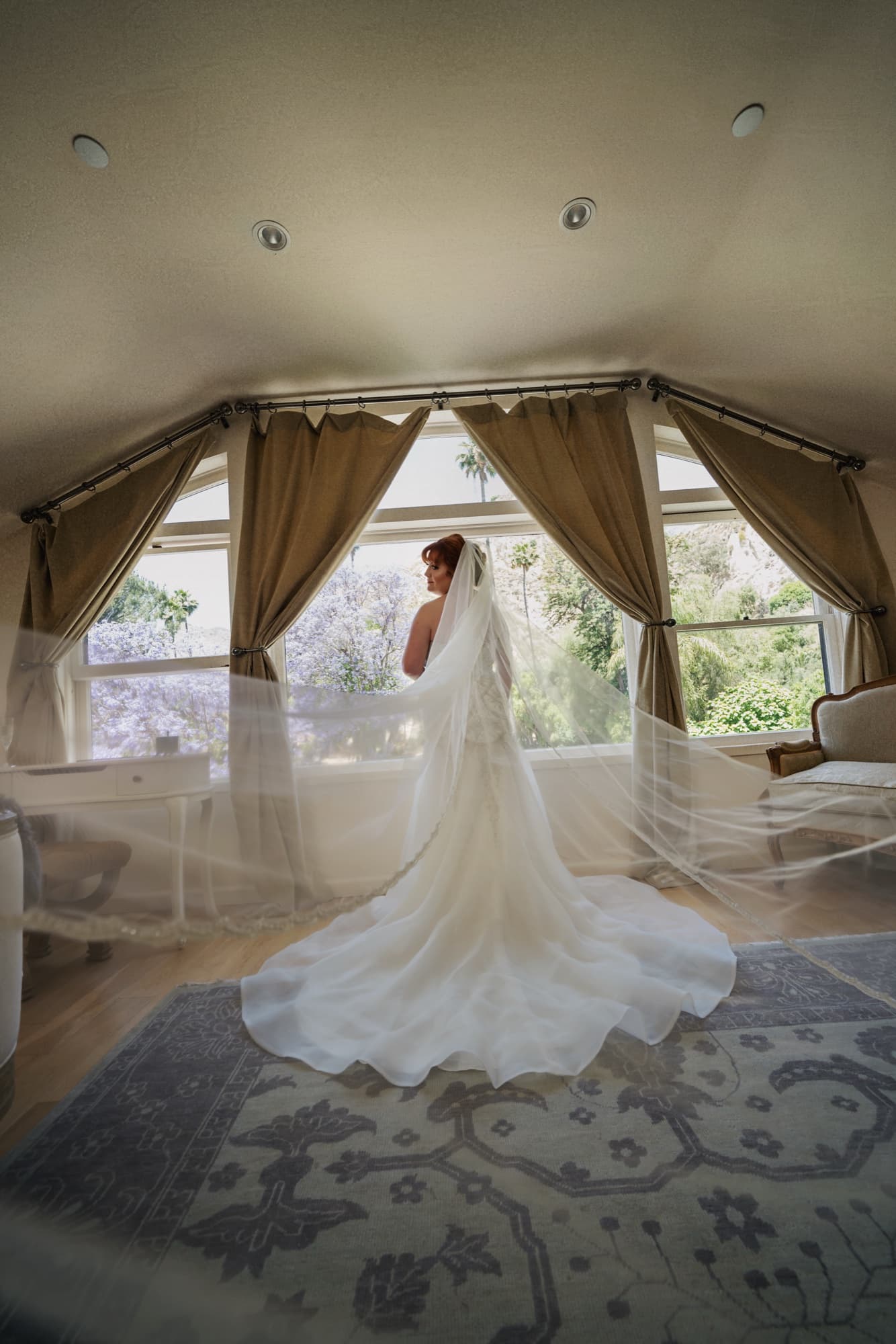 Michelle at the bay window in her beaded lace gown, the cathedral veil and train spilling across the antique rug