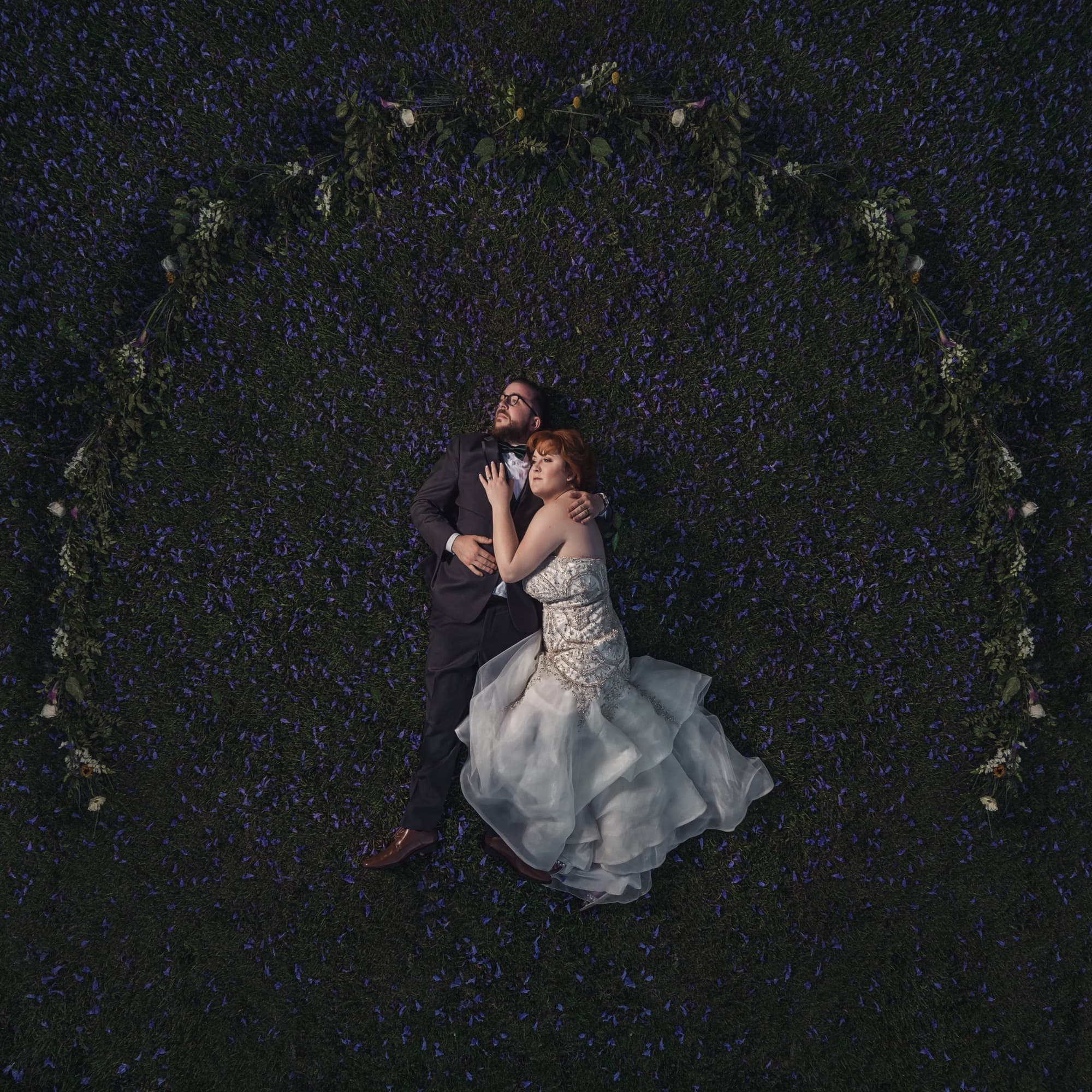 Overhead photograph of Michelle and Adam lying together inside a circular wreath of vines on the lawn at night
