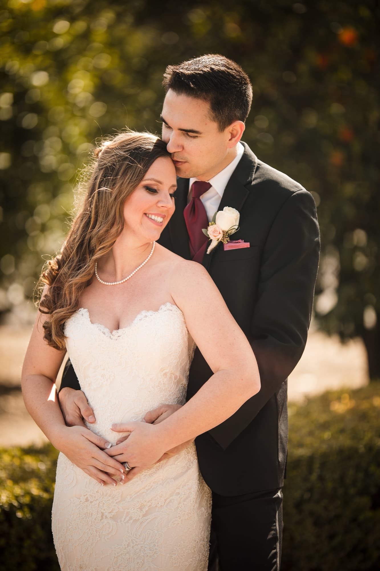 Tommy embracing Cathryn from behind in the golden-hour light of the orchard at Newhall Mansion
