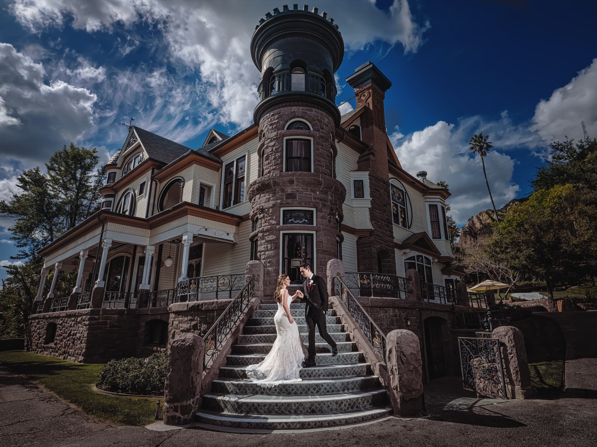 Cathryn and Tommy on the grand staircase of Newhall Mansion with the stone turret and dramatic sky above them